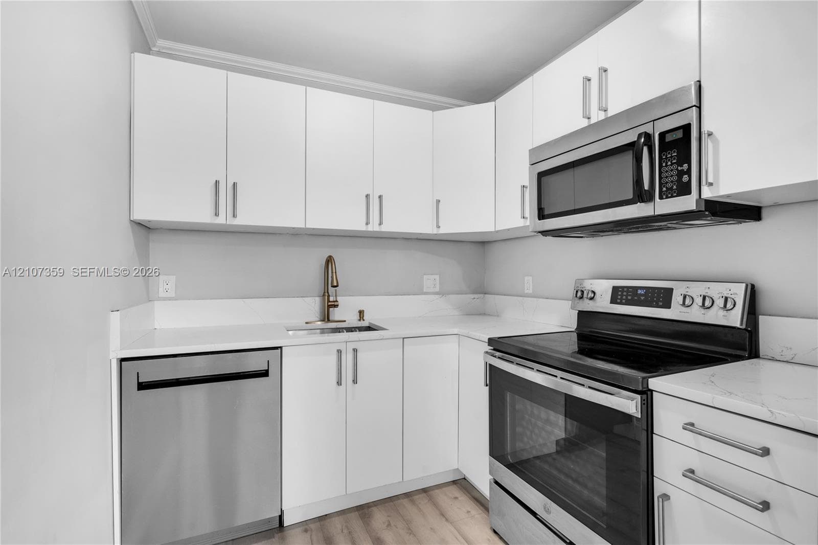 Kitchen featuring white shaker-style cabinetry, solid-surface countertops, and stainless steel appliances including an over-the-range microwave