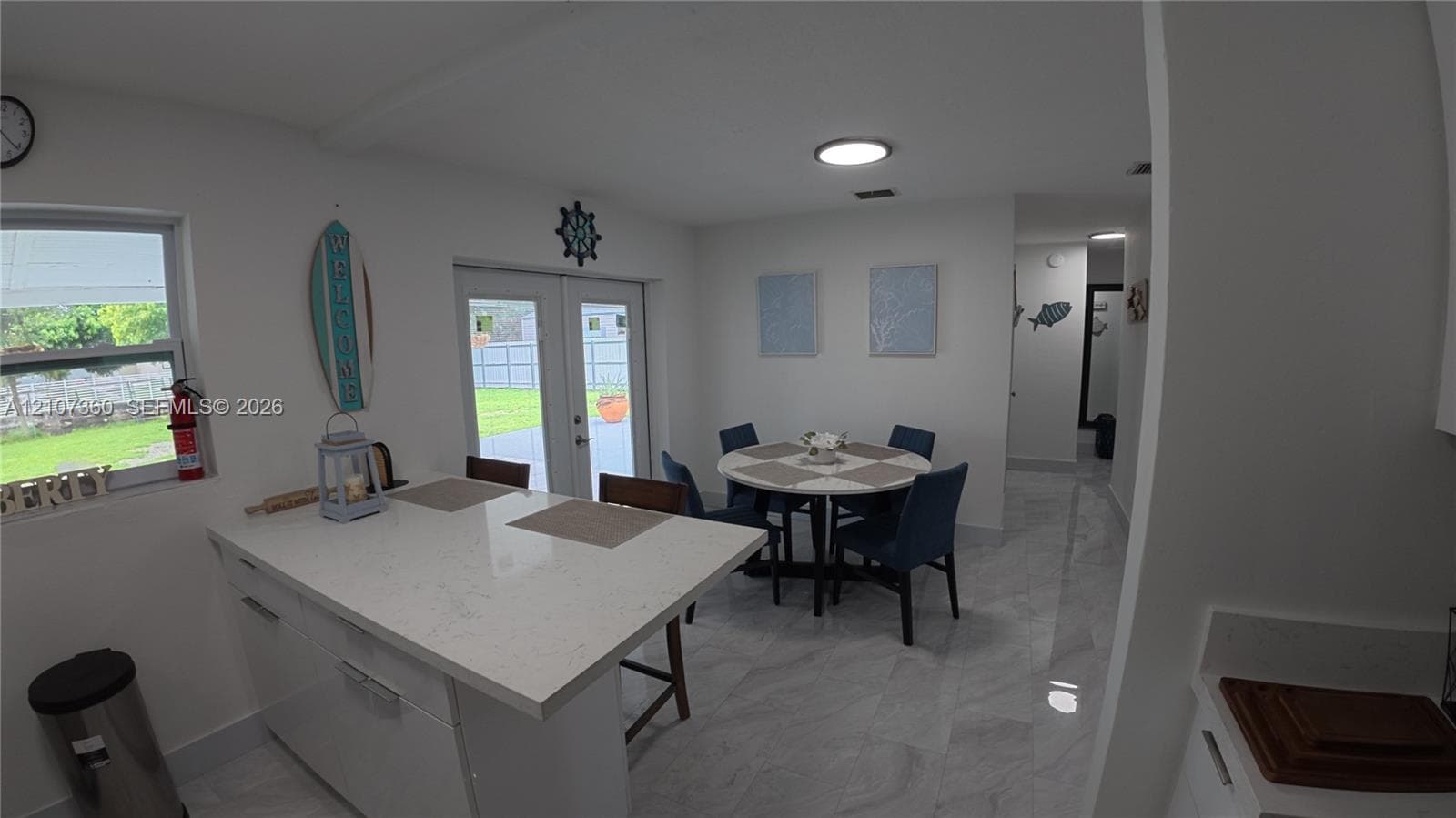 Kitchen area featuring white cabinetry, a quartz countertop island with integrated seating space, stone-finish flooring, and double glass doors providing exterior access