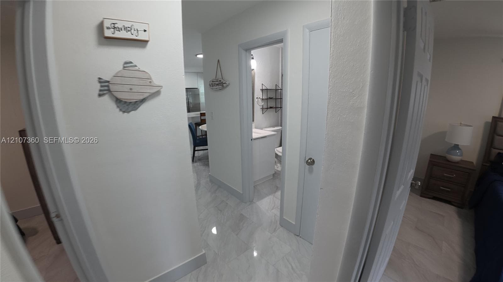 Interior hallway featuring large-format tile flooring, crisp white walls, and a recessed doorway providing entry to a bathroom equipped with a white vanity and stone-finish countertop