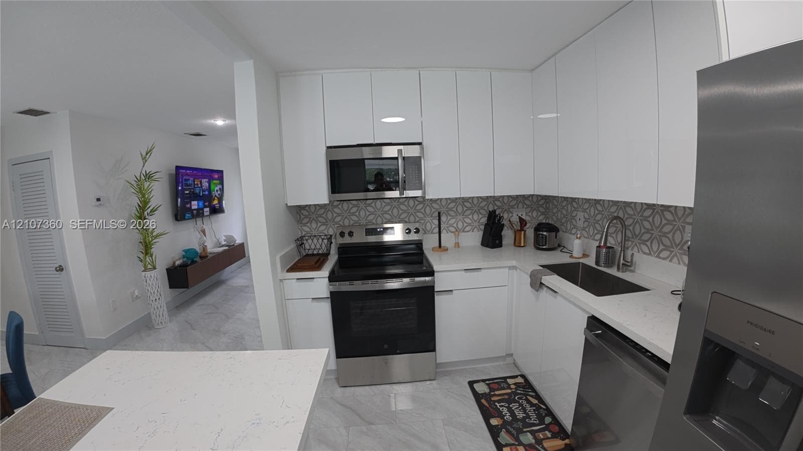 Kitchen featuring white flat-panel cabinetry, light-toned stone-finish countertops, stainless steel appliances, patterned tile backsplash, and light-toned tile flooring