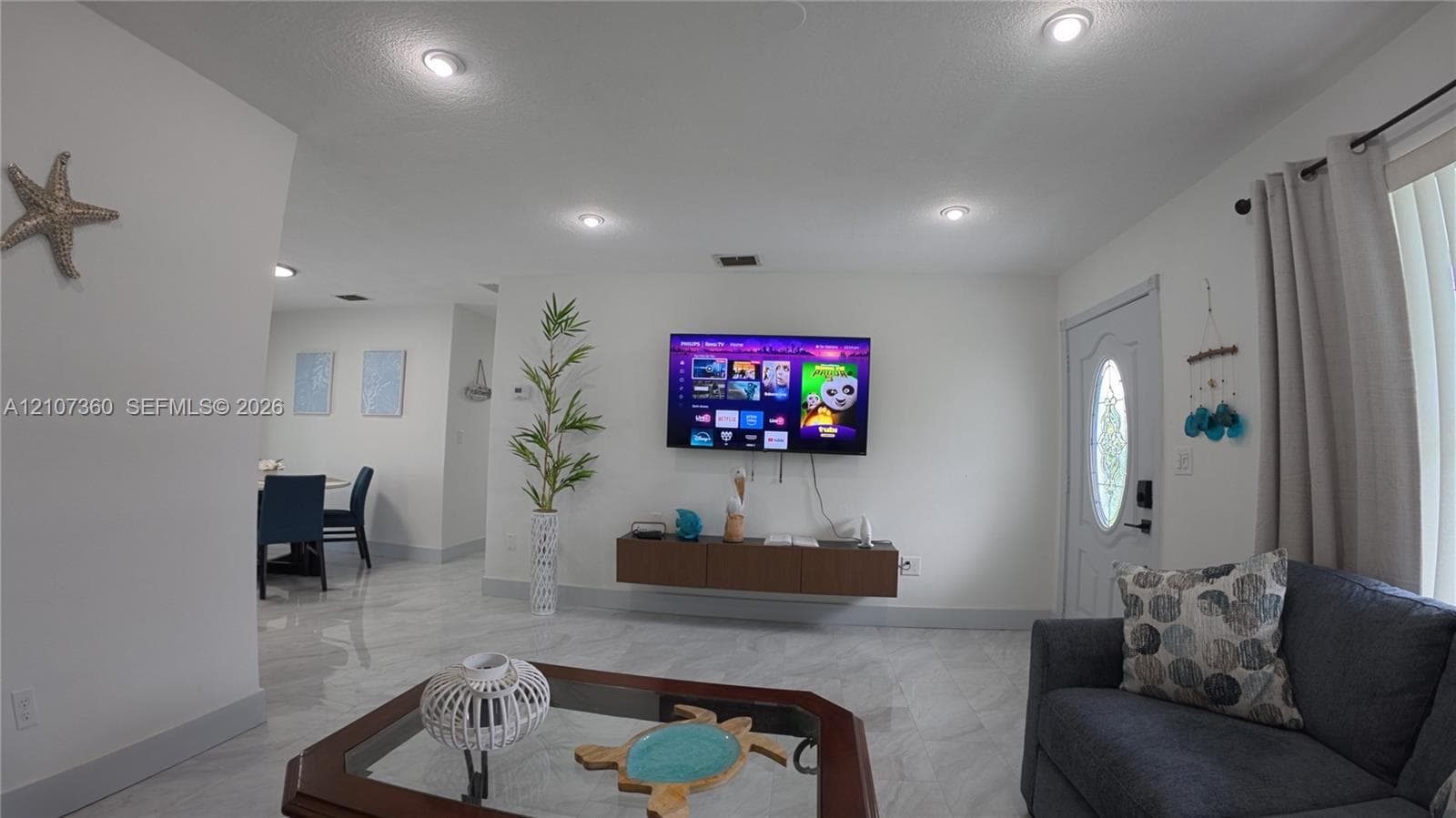 Living area featuring large-format tile flooring, recessed ceiling lighting, and a wall-mounted floating cabinet