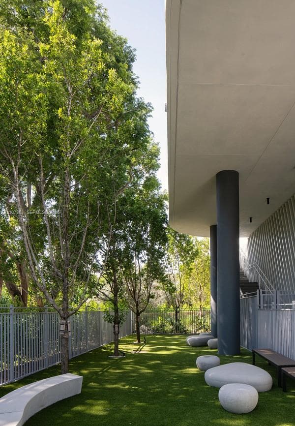 Covered outdoor space featuring cylindrical structural columns, artificial turf, perimeter metal fencing, and built-in stone-finish seating
