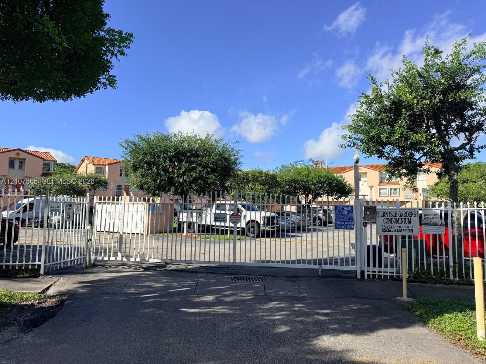 Gated entrance featuring white metal security fencing and asphalt driveway access