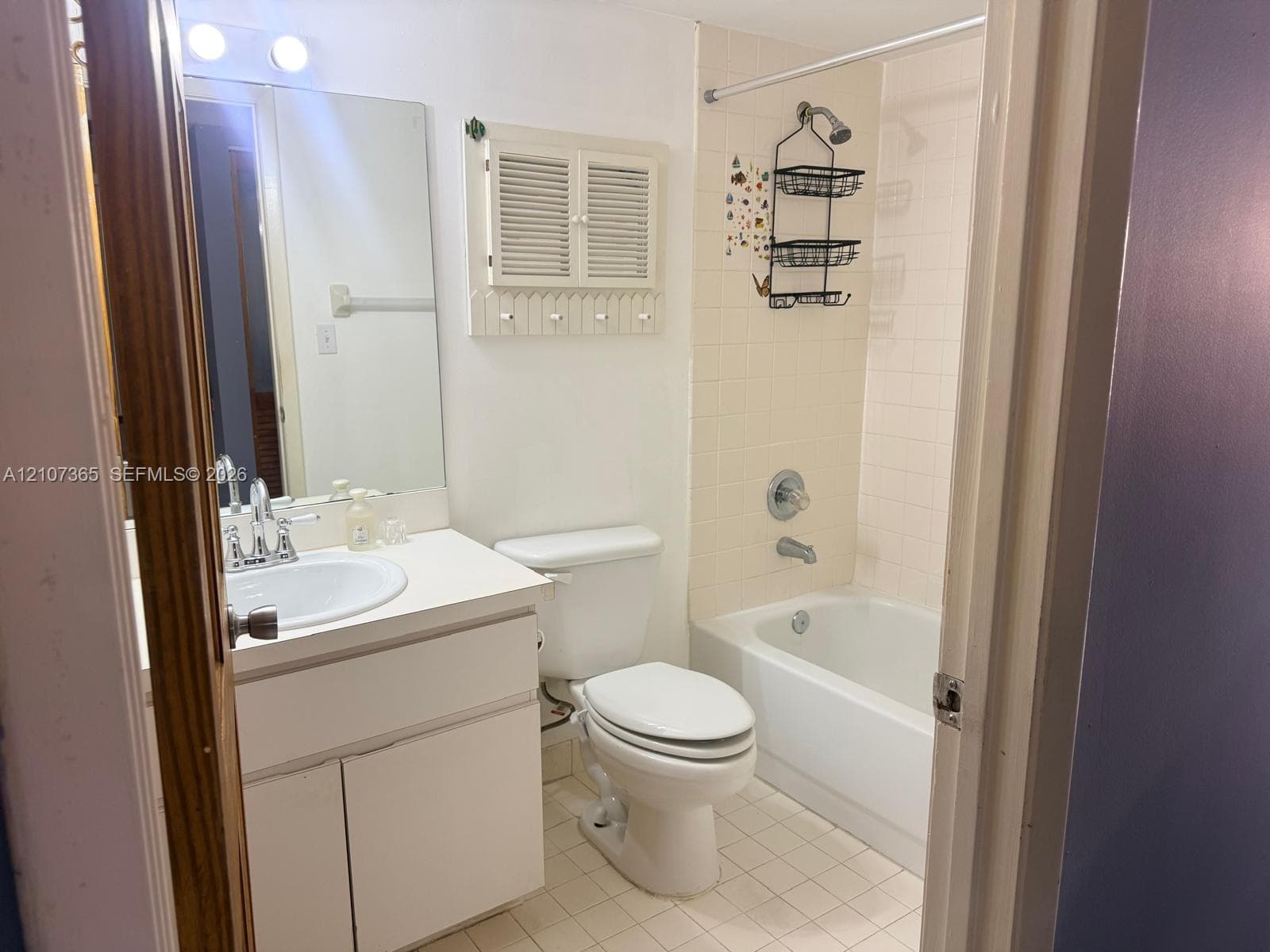 Bathroom featuring a white vanity cabinet with an integrated sink, wall-mounted medicine cabinet with louvered doors, oversized vanity mirror, and a tub-shower combination with tile surround