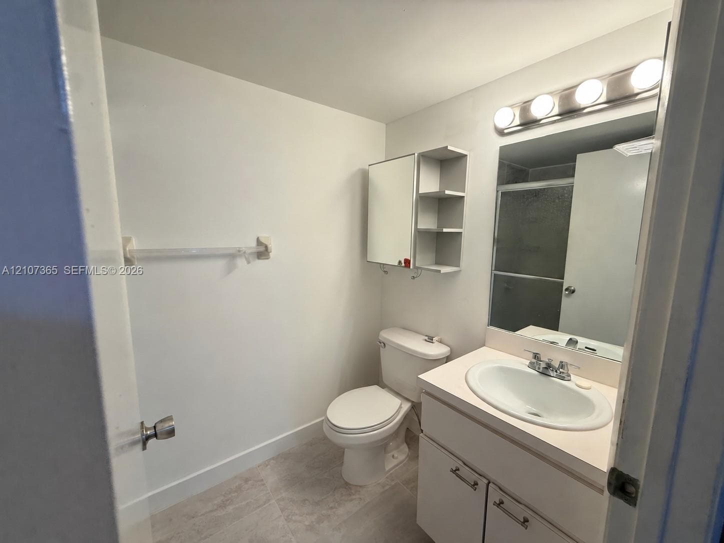 Bathroom featuring a vanity with integrated sink, wall-mounted medicine cabinet with open shelving, tile flooring, and a multi-bulb light fixture above the mirror