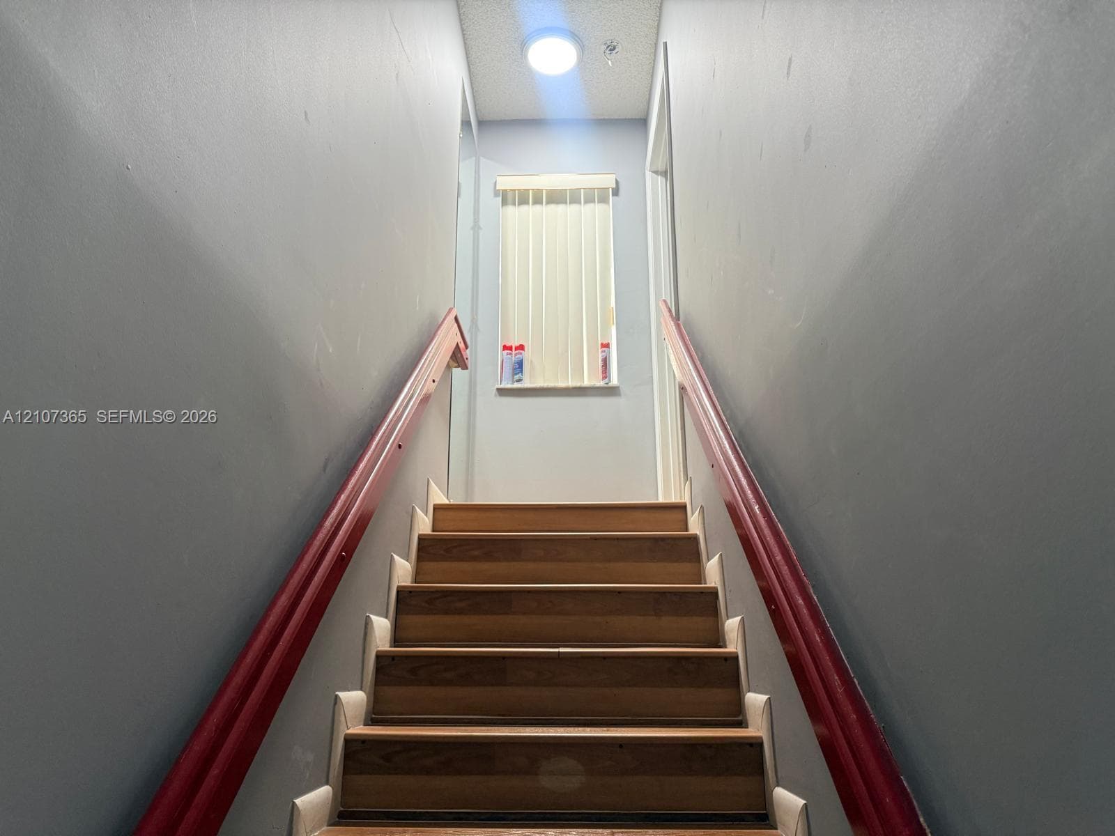 Staircase featuring wood-finish treads, dual wood-tone handrails, and a vertical blind window treatment