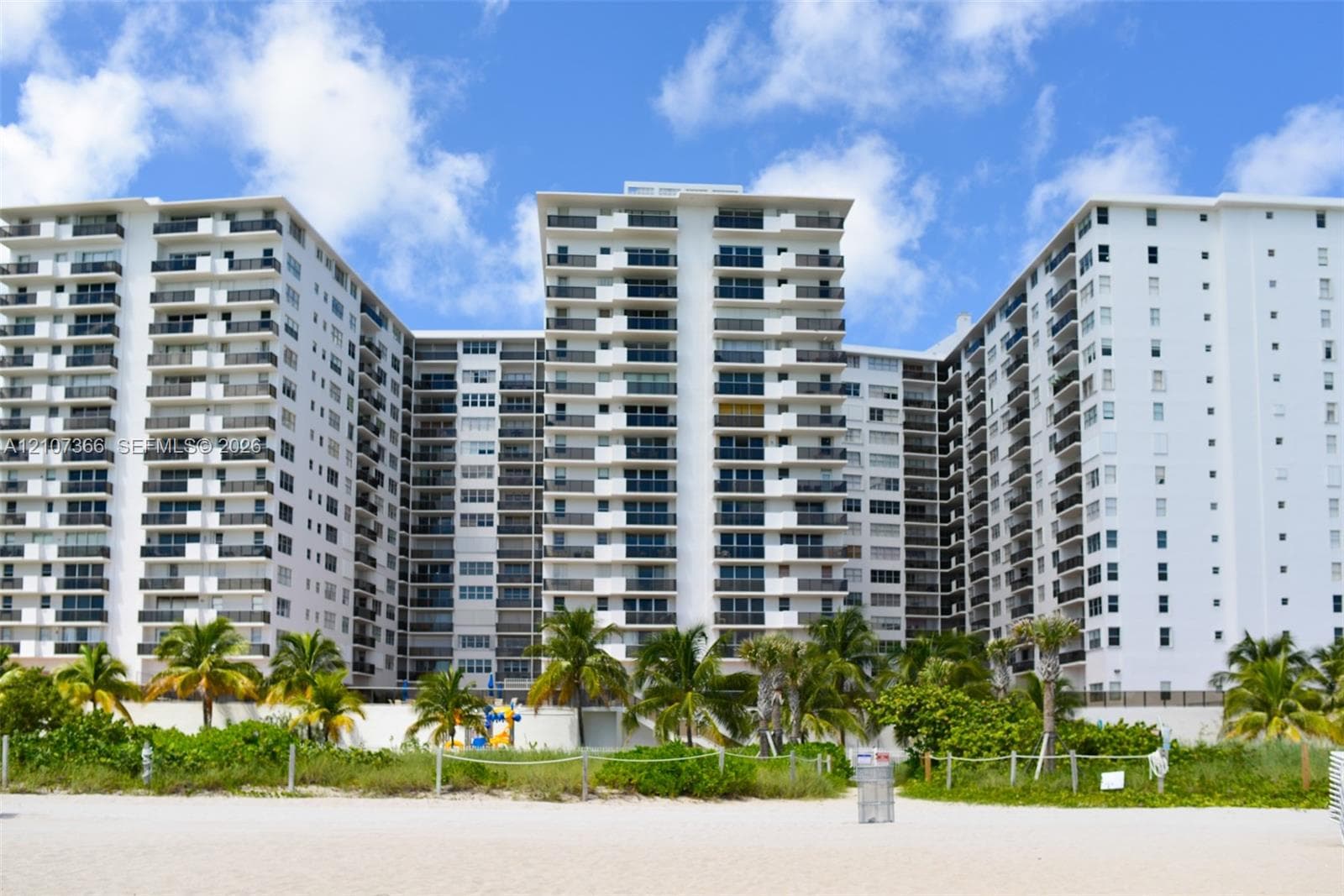 High-rise building featuring private balconies, floor-to-ceiling windows, and direct beach access surrounded by mature palm trees