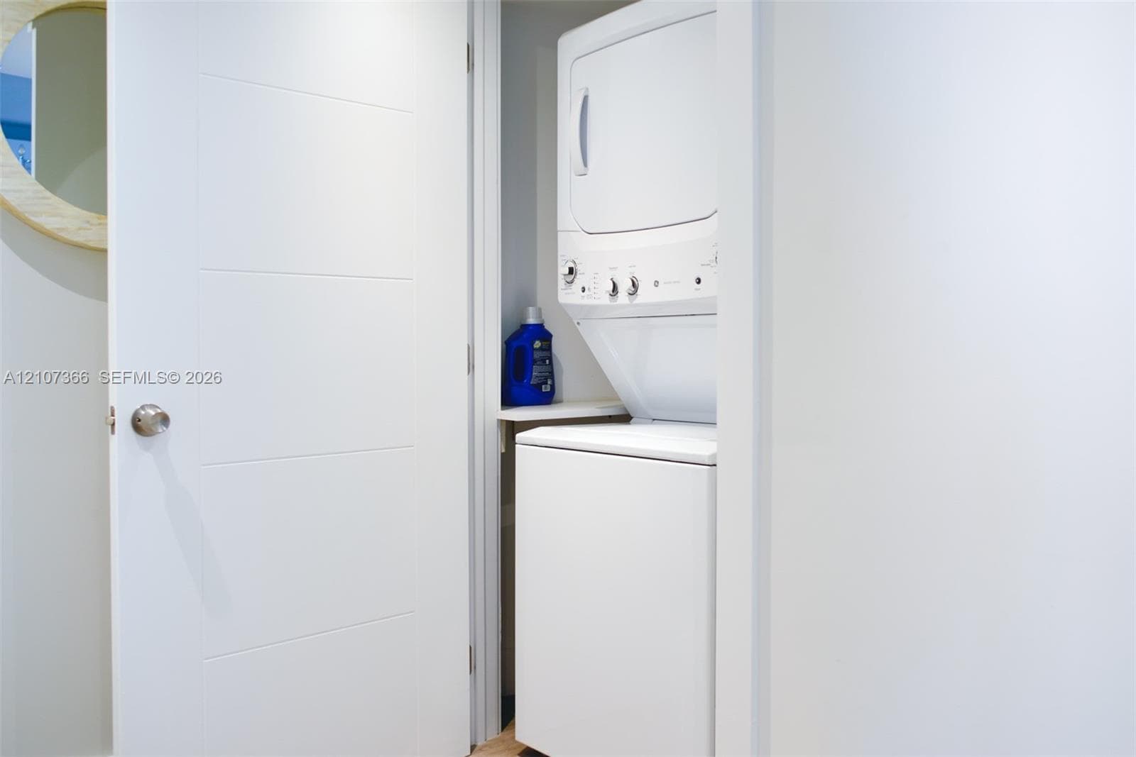 Stacked laundry unit featuring a white appliance finish and a built-in shelving ledge