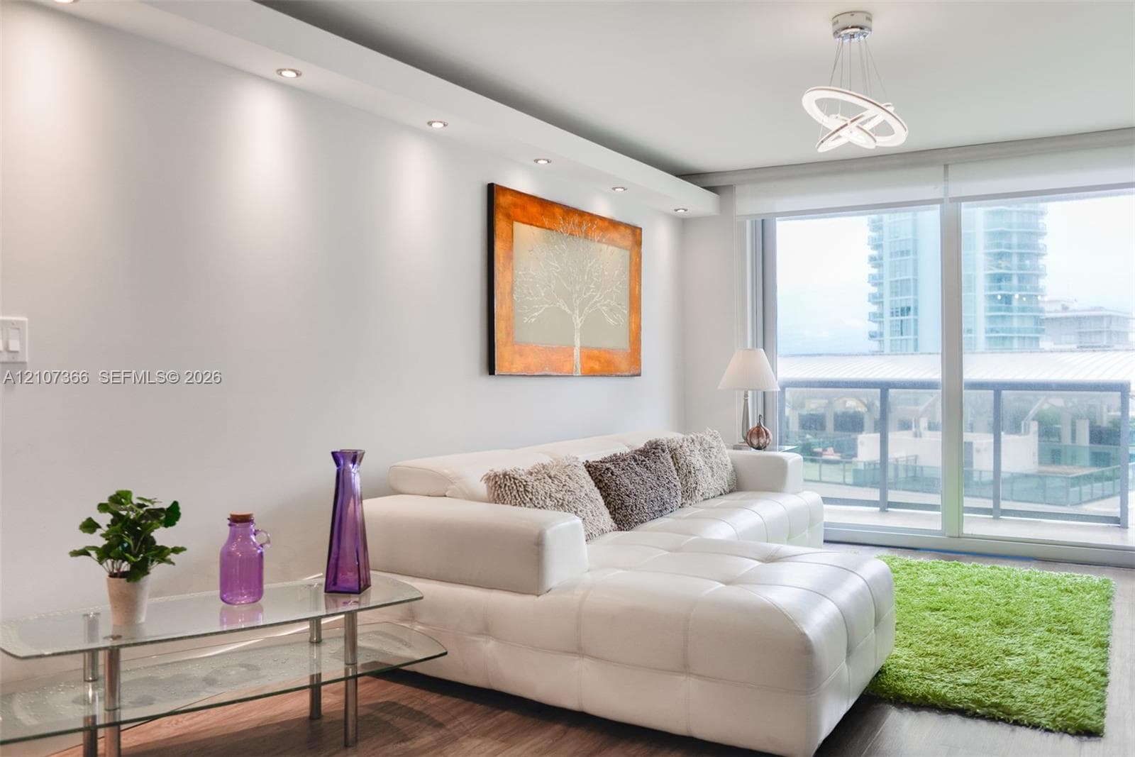 Living space featuring wood-finish flooring, recessed ceiling lighting, a contemporary LED chandelier, and floor-to-ceiling windows with balcony access