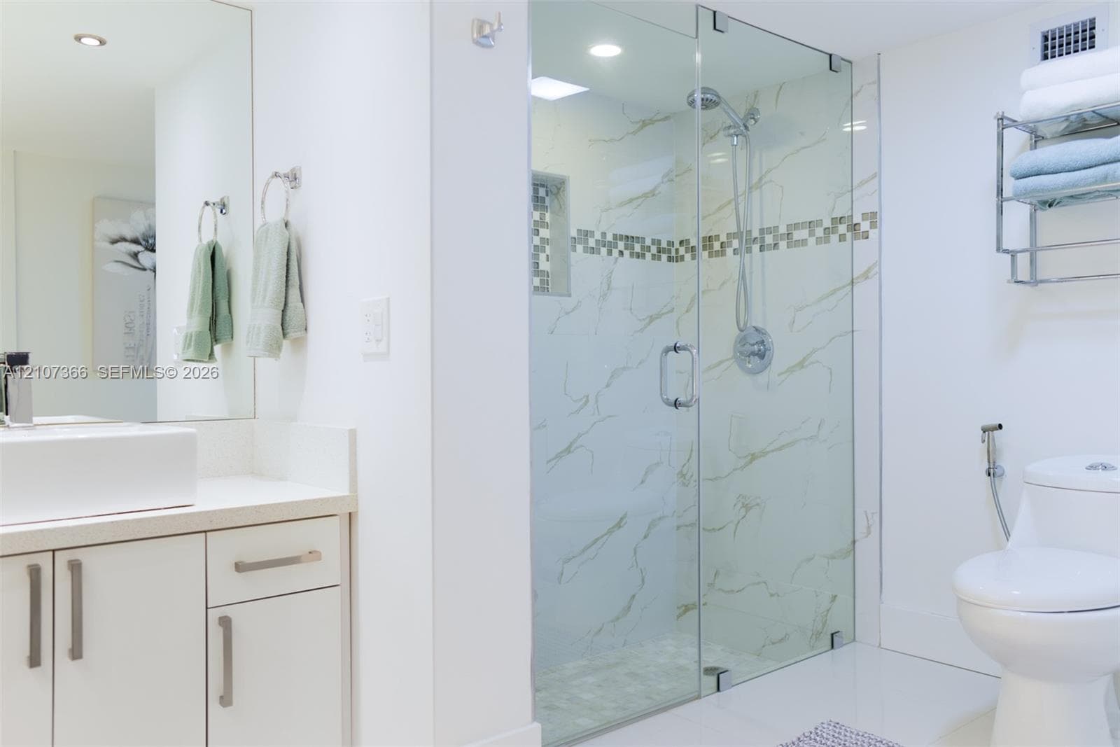 Bathroom featuring a glass-enclosed shower with tiled surround and decorative inlay, rectangular vessel sink, solid-surface countertop, and wall-mounted vanity storage