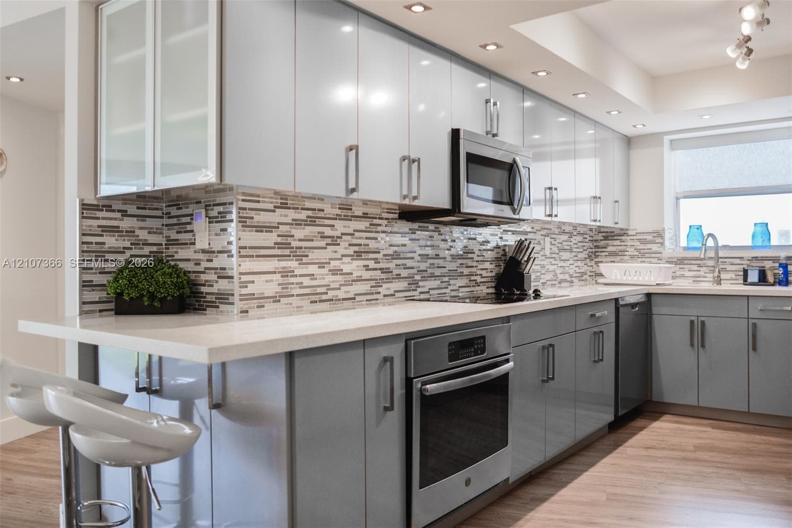 Kitchen featuring high-gloss cabinetry, stone-finish countertops, stainless steel appliances, multi-tonal linear tile backsplash, and wood-finish flooring