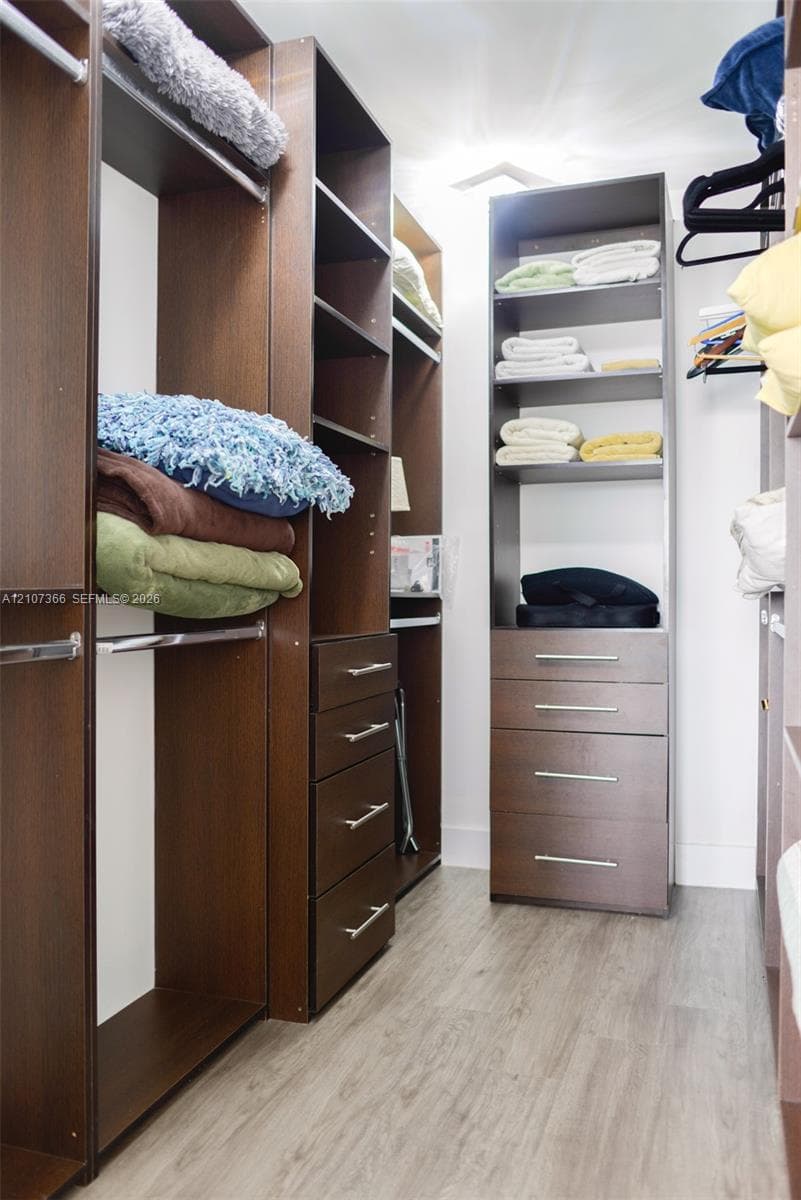 Custom closet organization system featuring dark wood-finish cabinetry, built-in shelving, integrated dresser drawers with brushed metal pulls, and wood-finish flooring