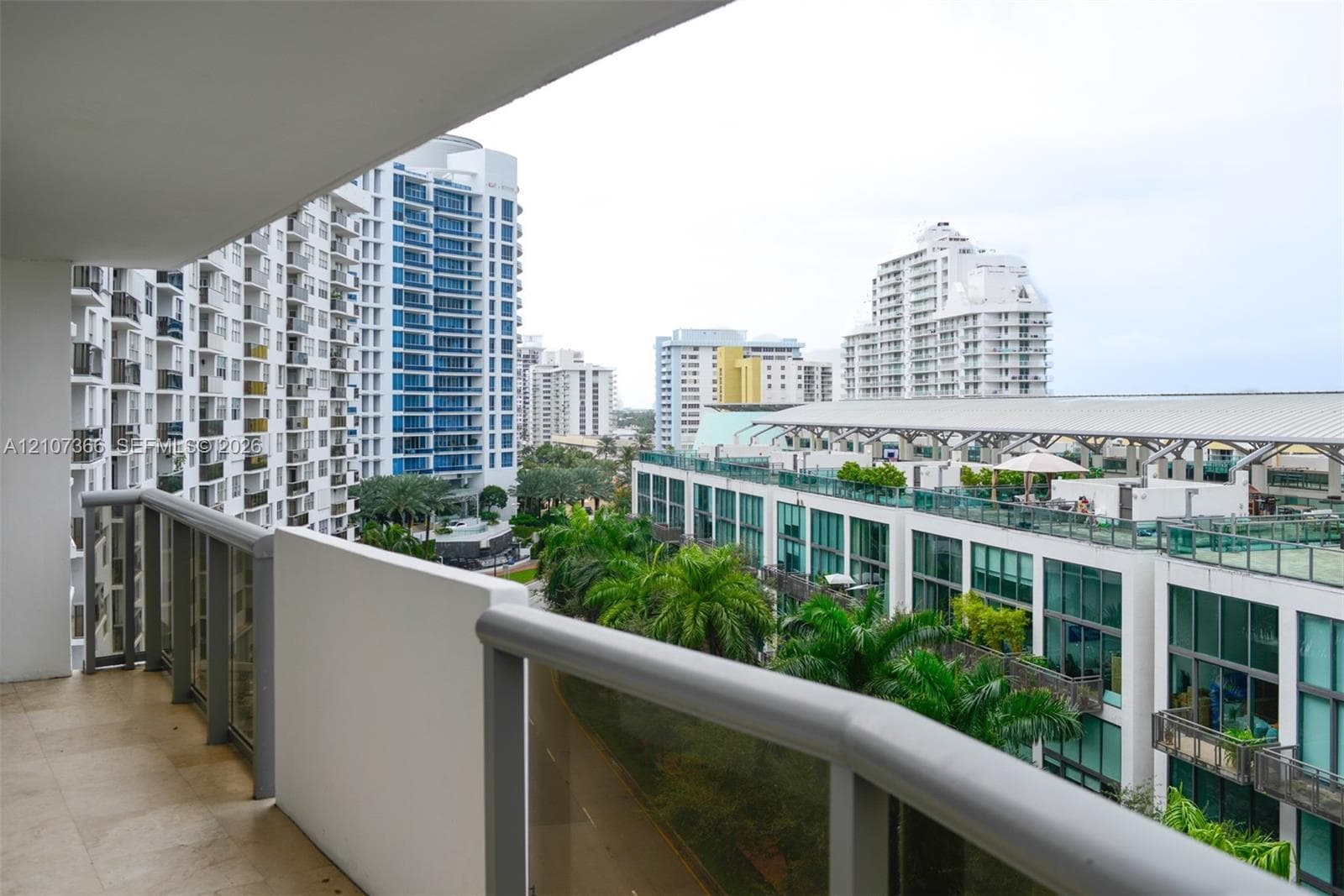 Covered balcony featuring stone flooring and metal-framed glass railings with urban surroundings