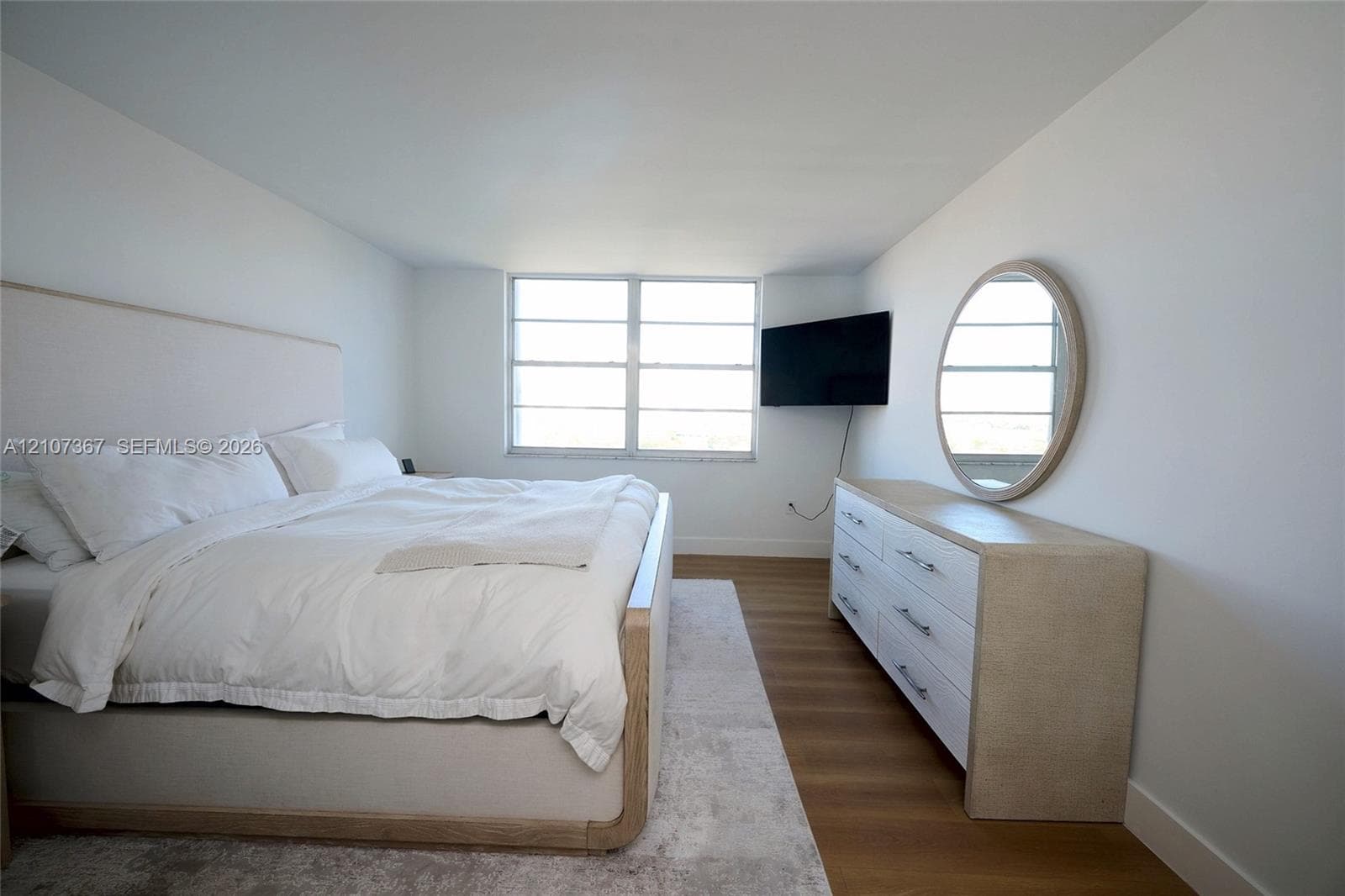 Custom closet featuring built-in white shelving, integrated hanging rods, tiered pull-out drawers, and wood-finish flooring