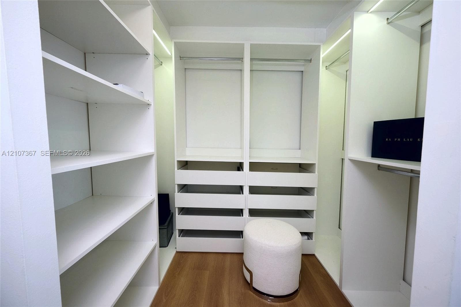 Bedroom featuring wood-finish flooring, built-in closet organization system with drawers, and wall-mounted shelving unit