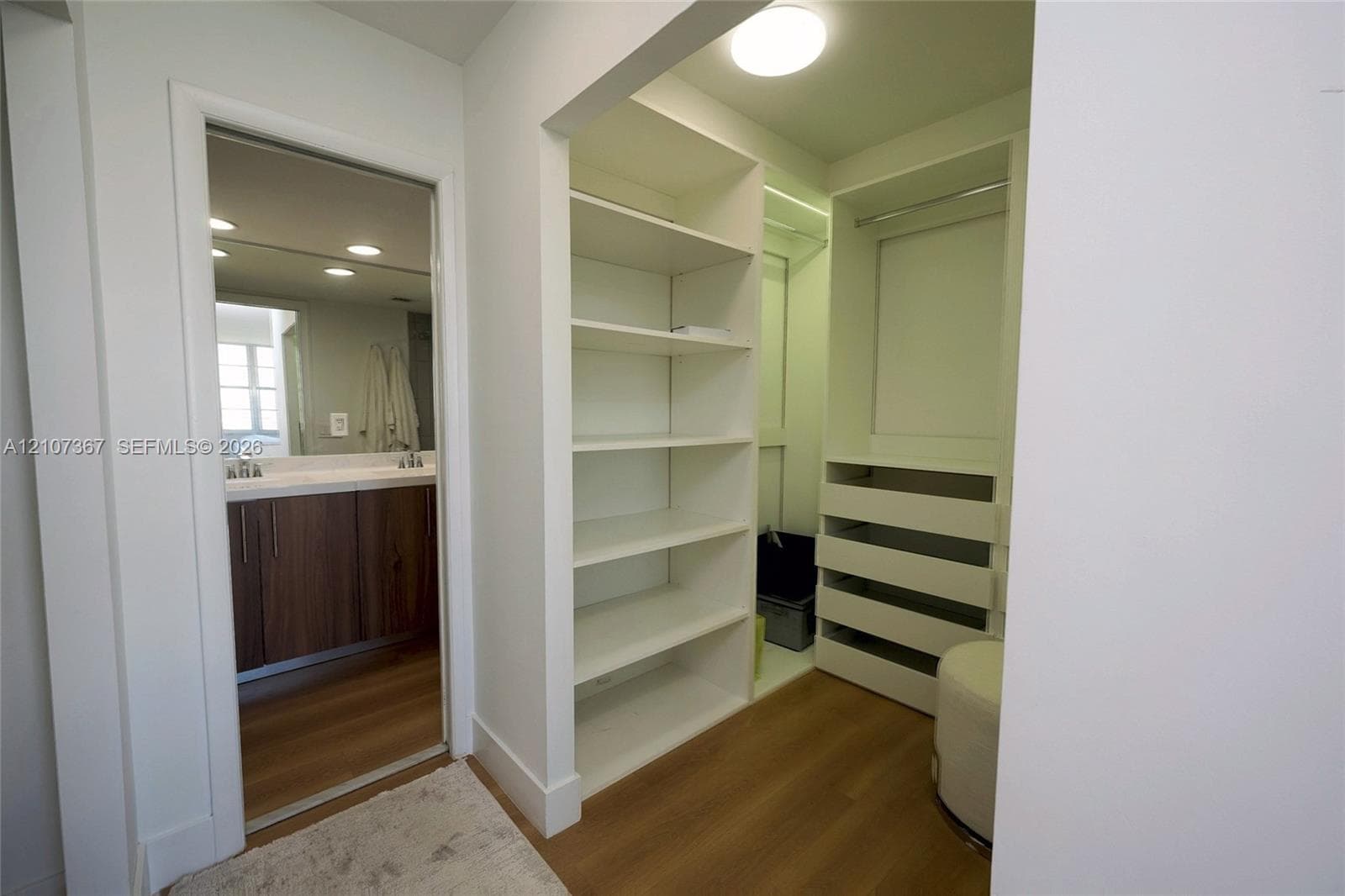 Double vanity with rectangular integrated sinks, wood-finish cabinetry, full-width mirror, and walk-in shower featuring a tiled bench seat