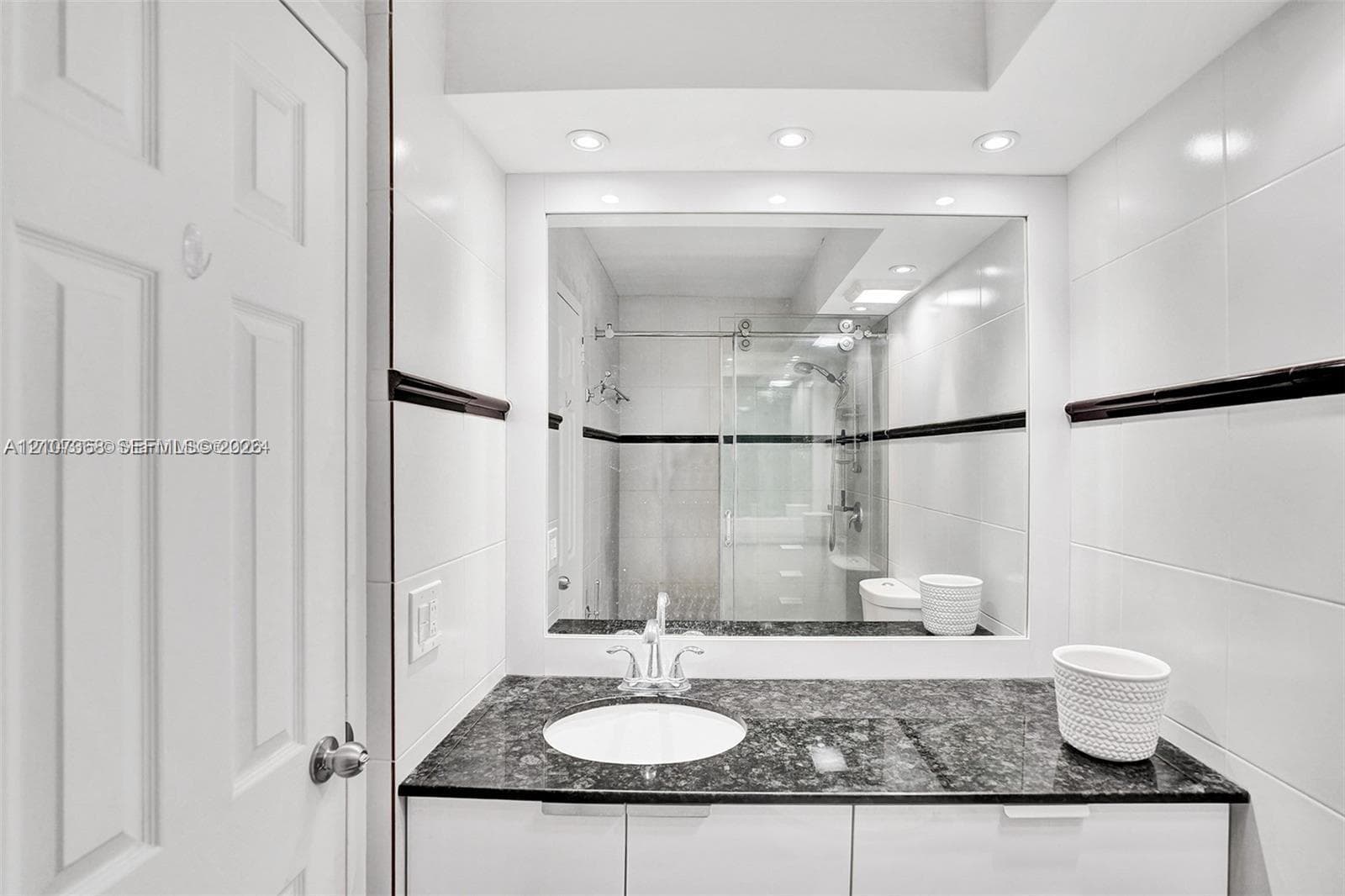 Bathroom featuring a stone-surface vanity with an integrated basin, high-gloss white cabinetry, large-format wall tiling with a dark decorative accent border, and a glass-enclosed shower stall with sliding hardware