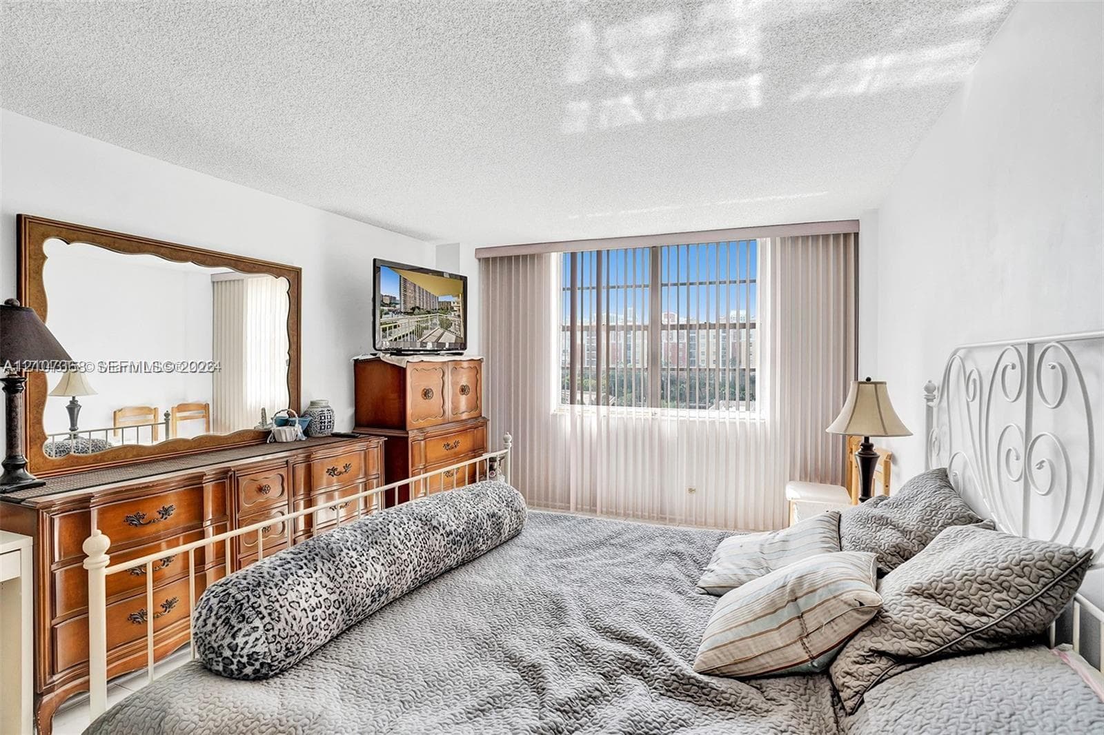 Bedroom featuring white walls, a textured ceiling, and a wide window with vertical blinds
