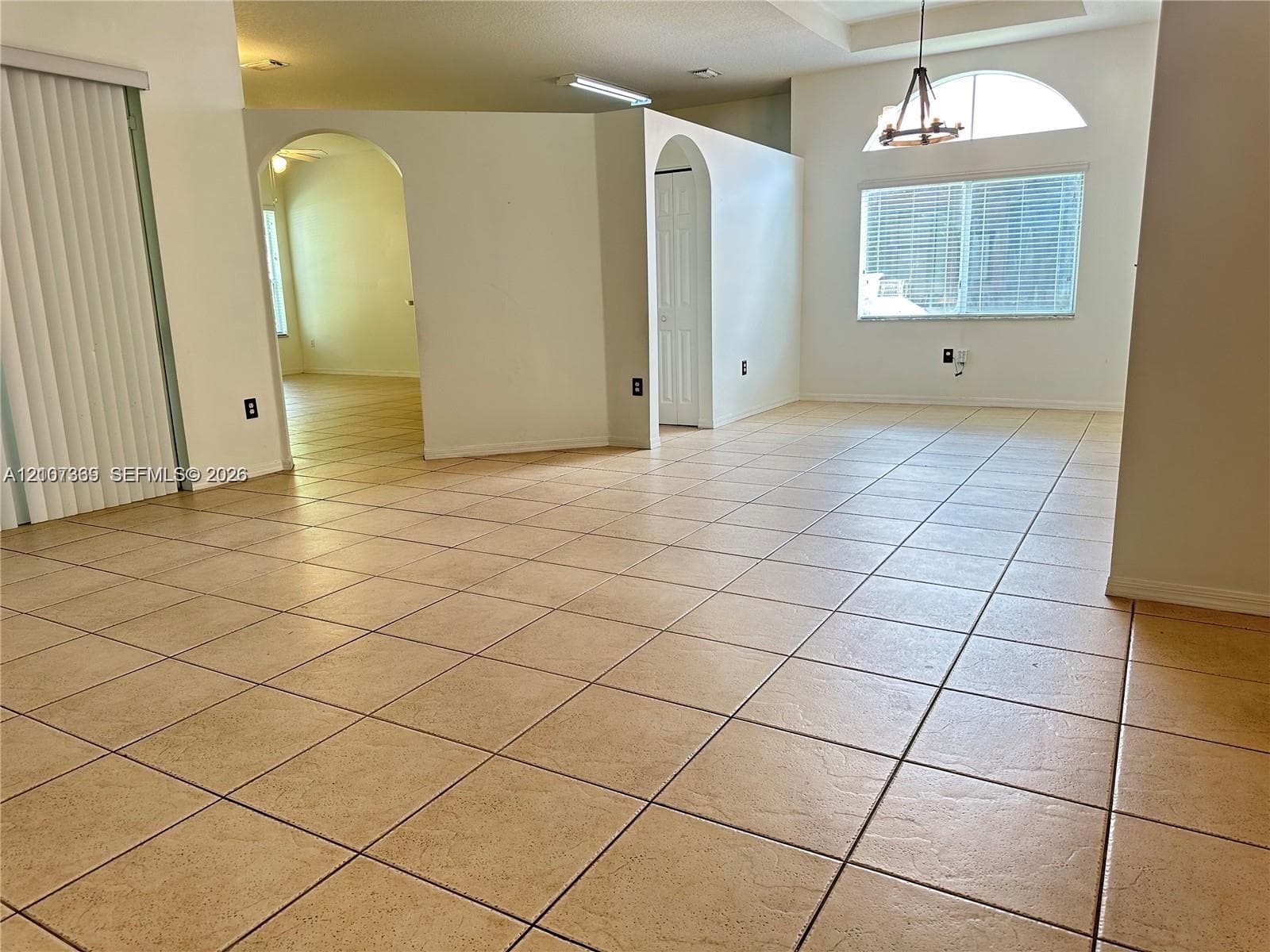 Open-concept interior featuring large-format tile flooring, vaulted ceilings, arched entryways, and an arched window with an integrated light fixture