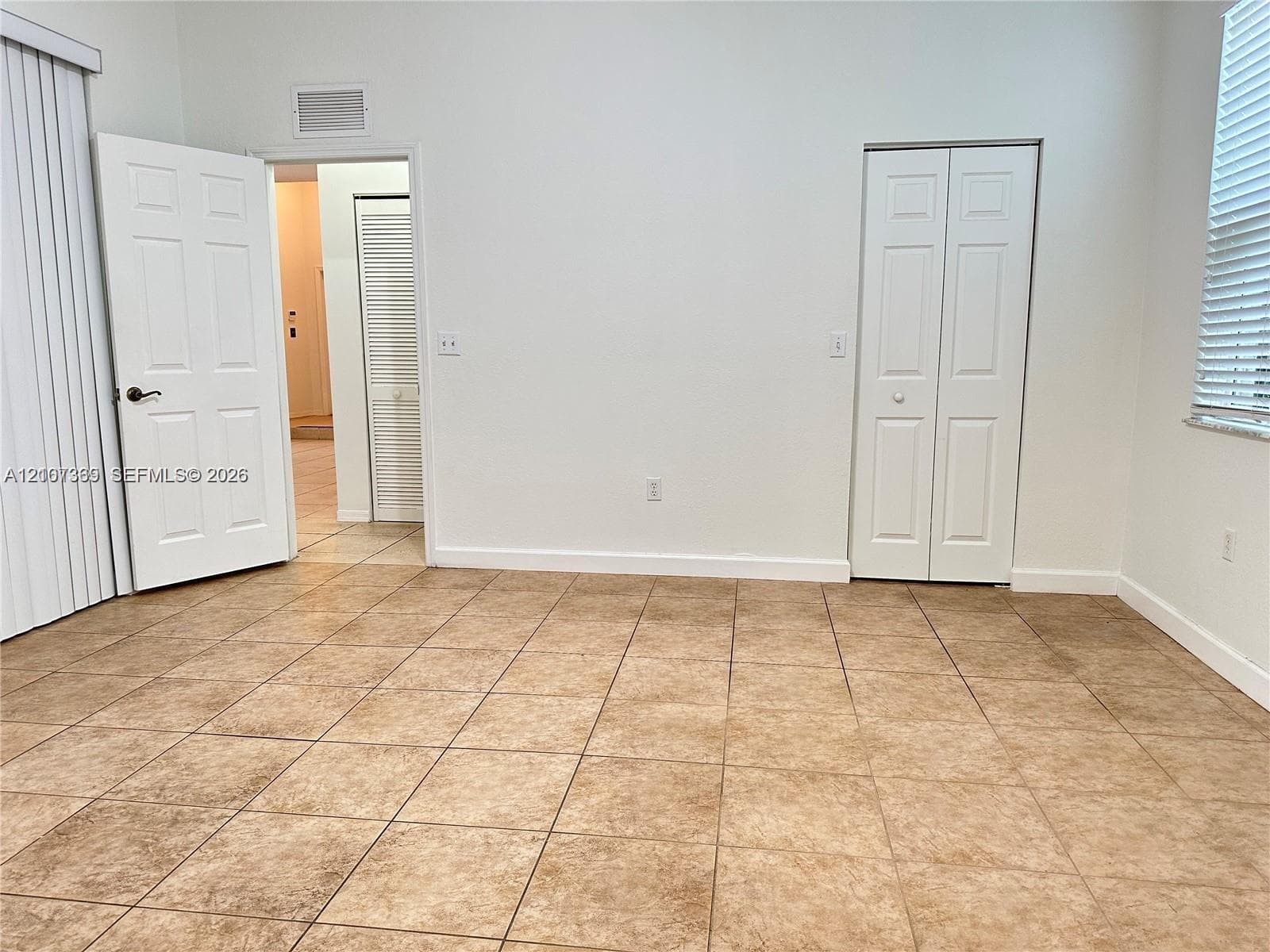 Neutral-toned ceramic tile flooring, dual-panel interior doors, and built-in closet storage with louvered and solid-panel doors