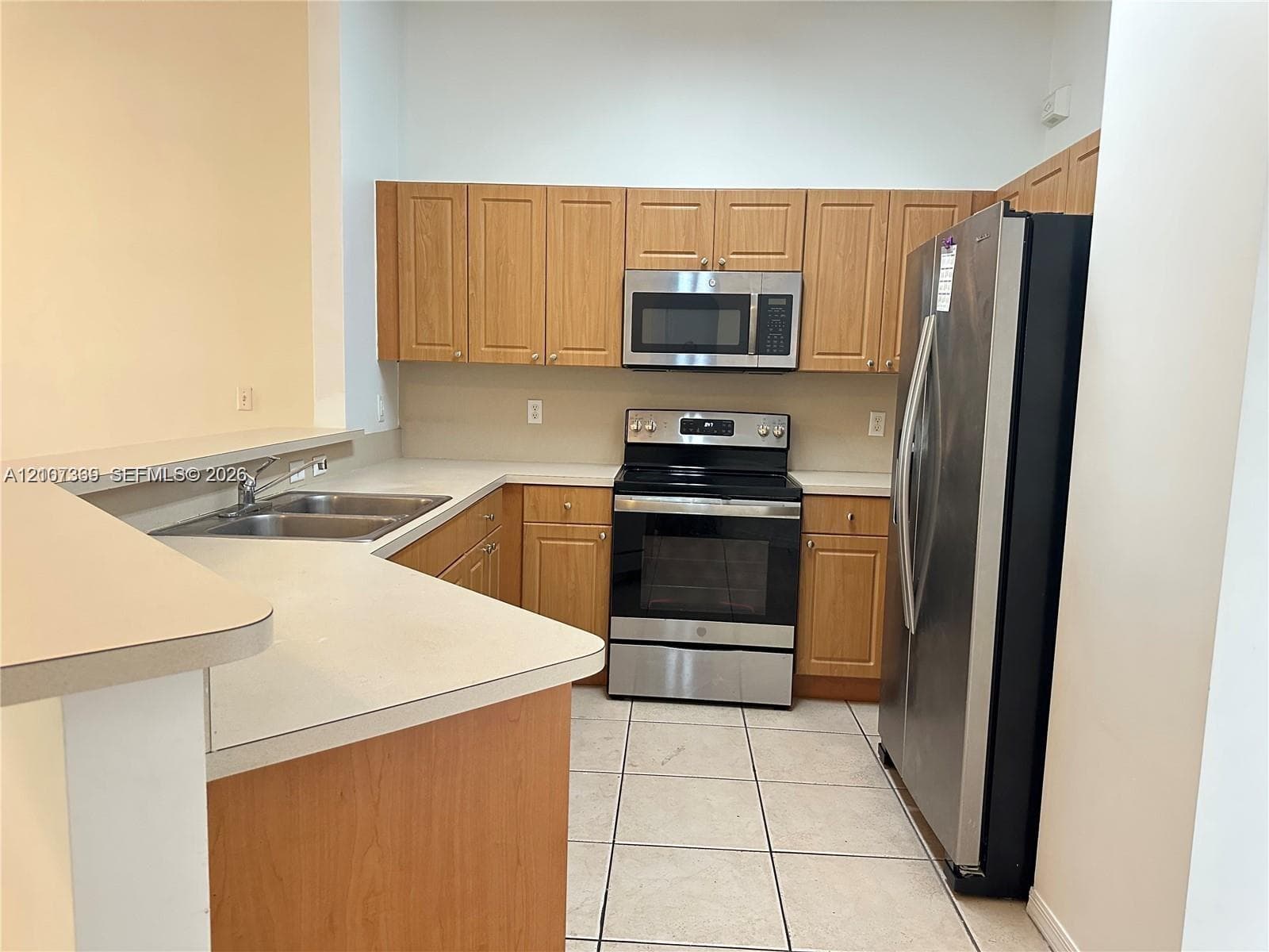 Kitchen featuring light-finish cabinetry, neutral solid-surface countertops, stainless steel appliances, a double-basin sink, and tile flooring