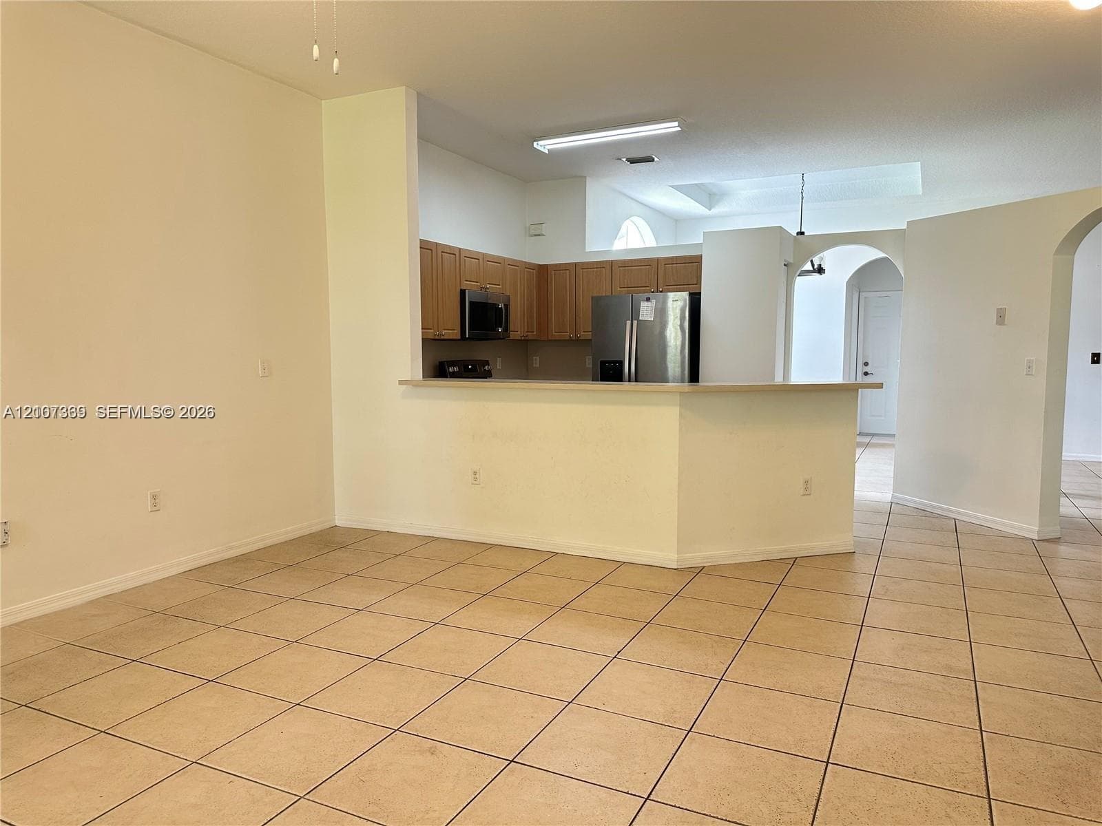 Kitchen featuring wood cabinetry, stainless steel appliances, and a breakfast bar, complemented by neutral tile flooring throughout