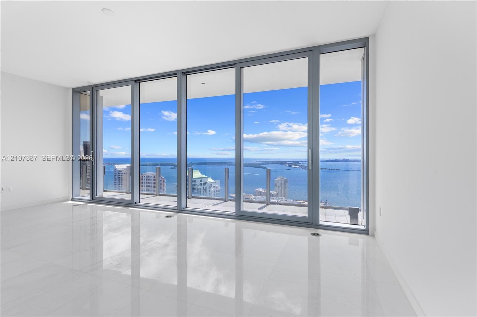 Floor-to-ceiling glass panel windows, sliding glass door, polished tile flooring, and private balcony with metal and glass railing