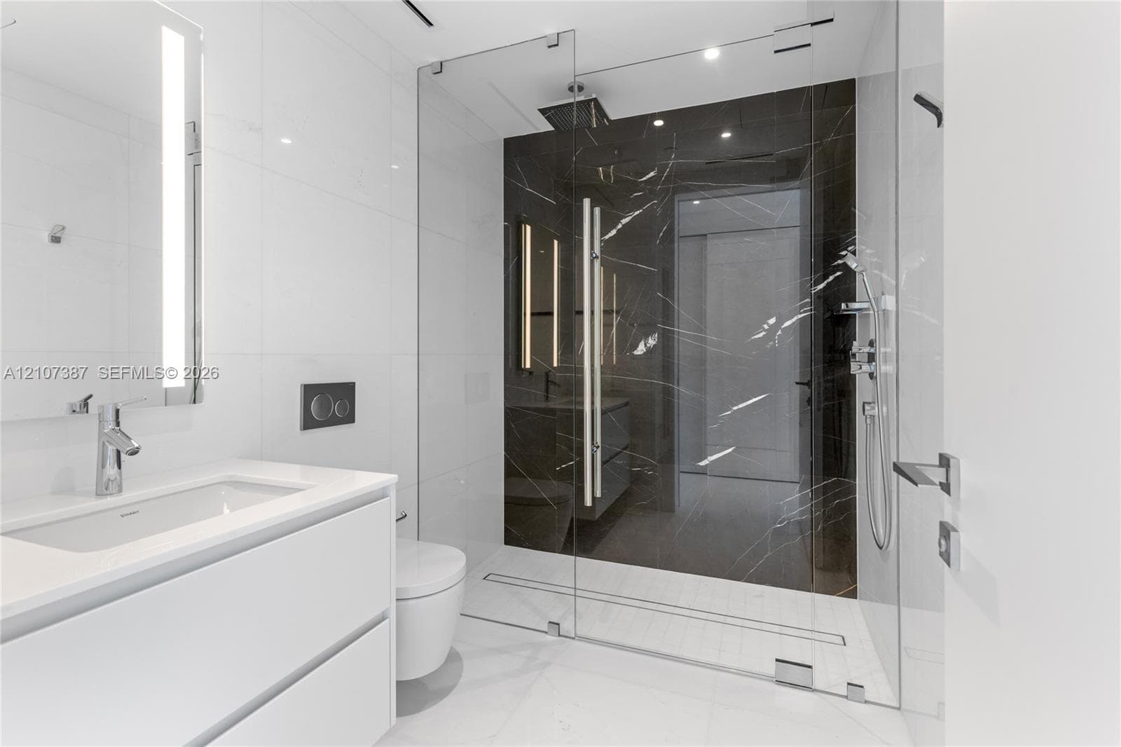 Modern bathroom featuring a floating white vanity with a rectangular sink, wall-mounted faucet, walk-in shower with floor-to-ceiling glass enclosure, dark stone-finish shower surround, and integrated lighting