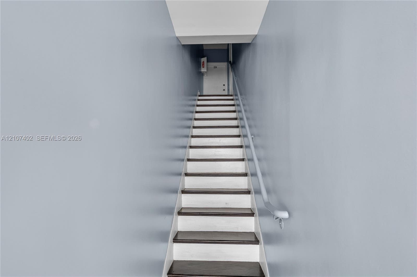 Staircase featuring dark-finished treads, white risers, and a wall-mounted handrail