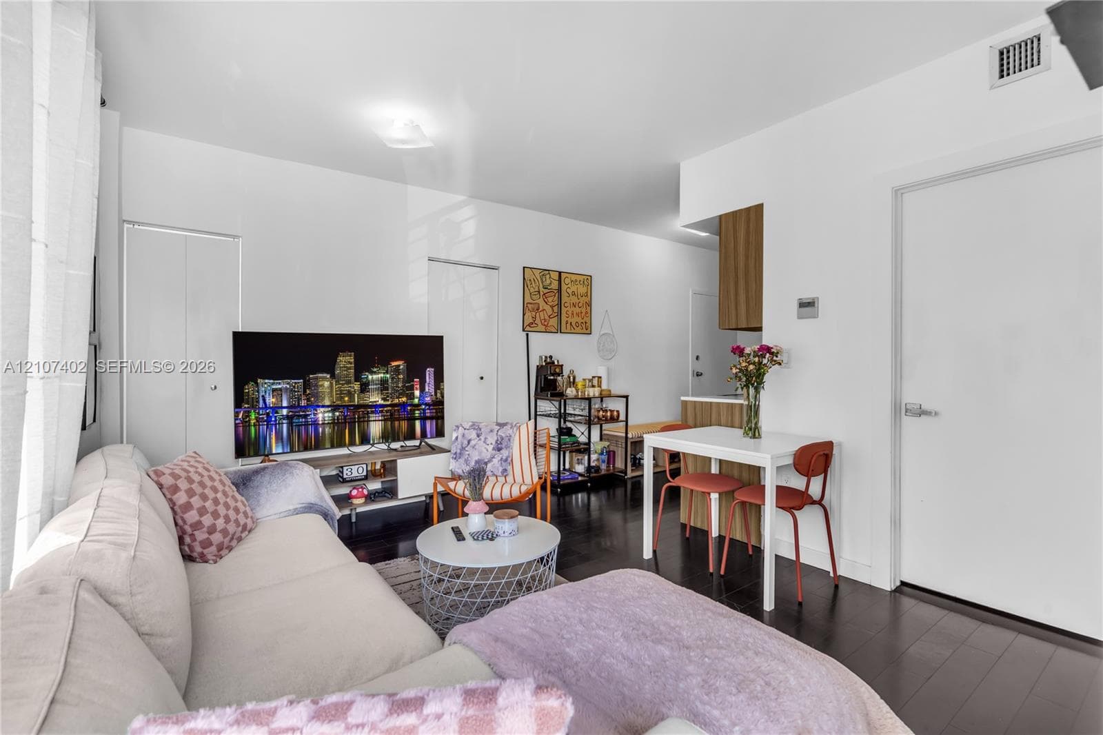 Open-concept living space featuring wood-finish flooring, crisp white walls, and built-in closet cabinetry
