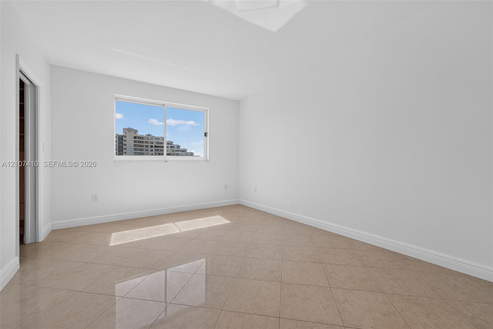 Bright room featuring neutral-toned tile flooring, white wall finishes, and a sliding window