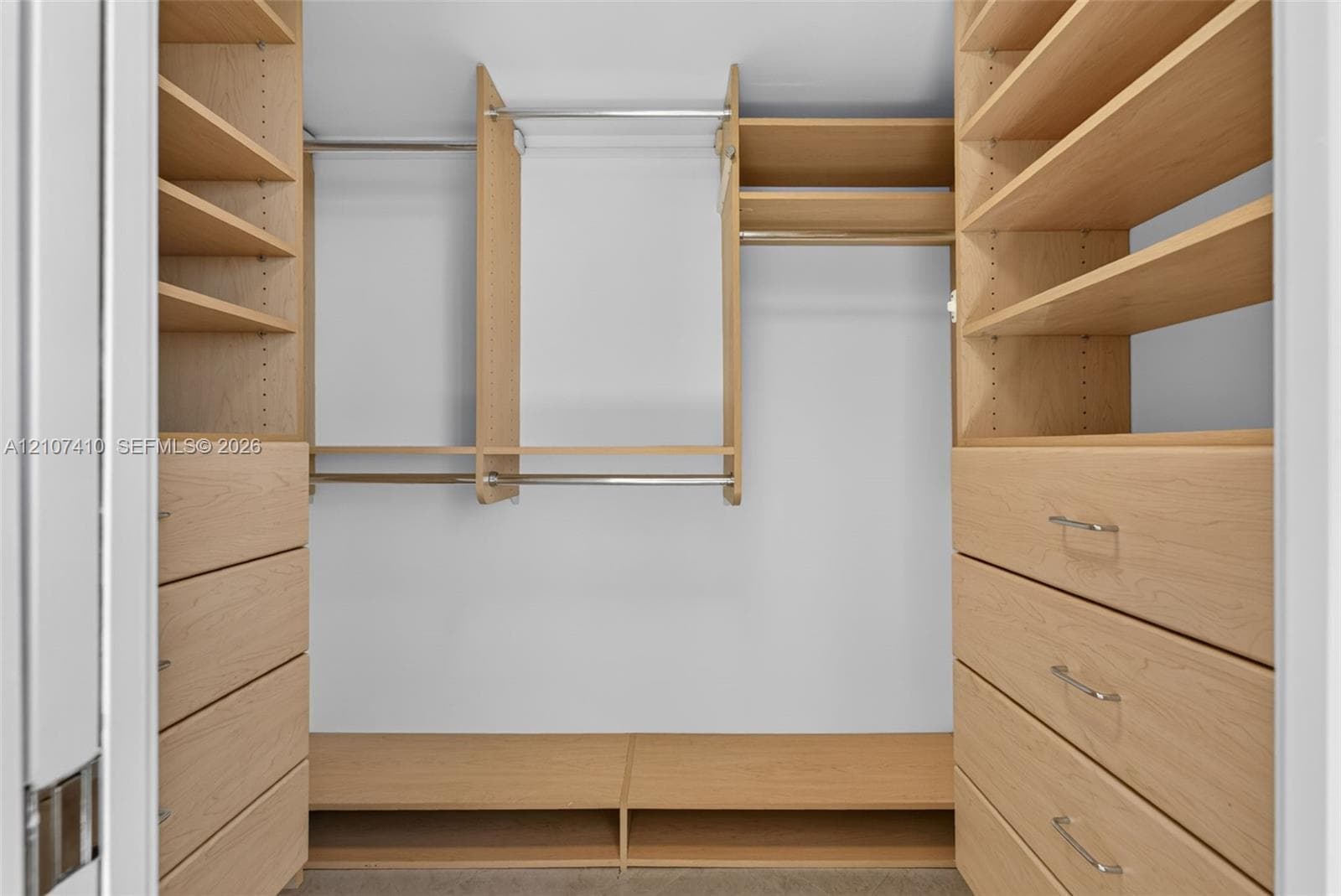 Custom walk-in closet featuring light-toned wood-finish cabinetry, built-in shelving units, integrated drawers with metallic pulls, and tiered hanging rods