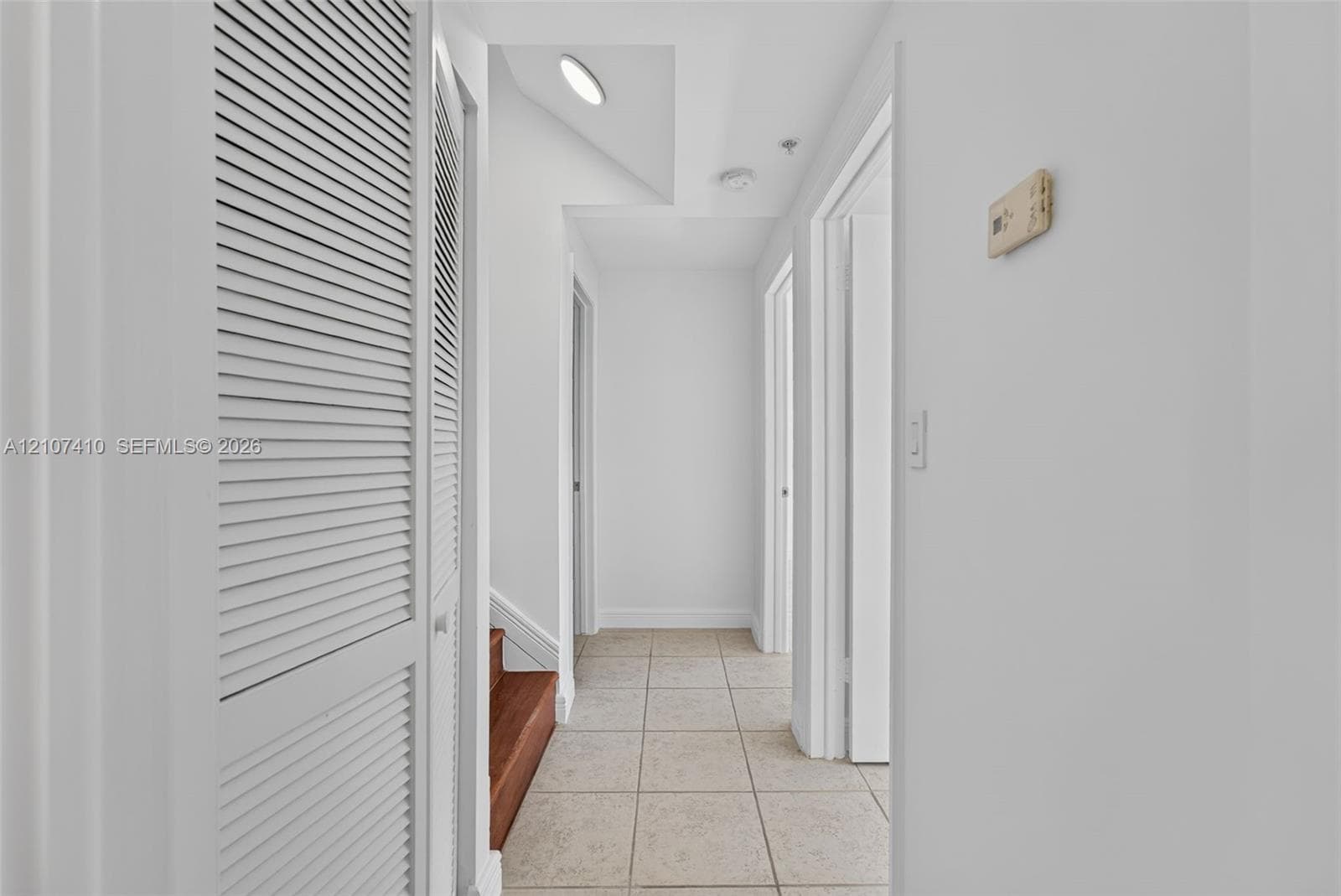 Hallway featuring white louvered-door closet, tile flooring, and wood-finish stairs