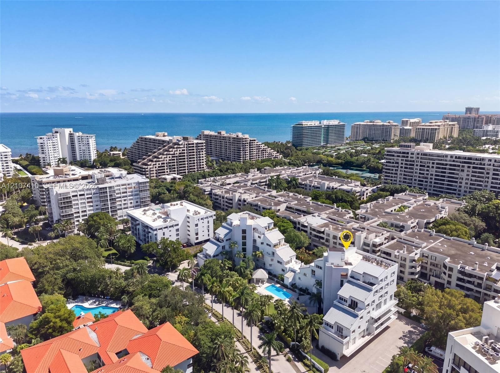 Aerial perspective of a multi-story residential complex featuring white architectural exteriors, multiple swimming pools, lush tropical landscaping, and proximity to the coastline