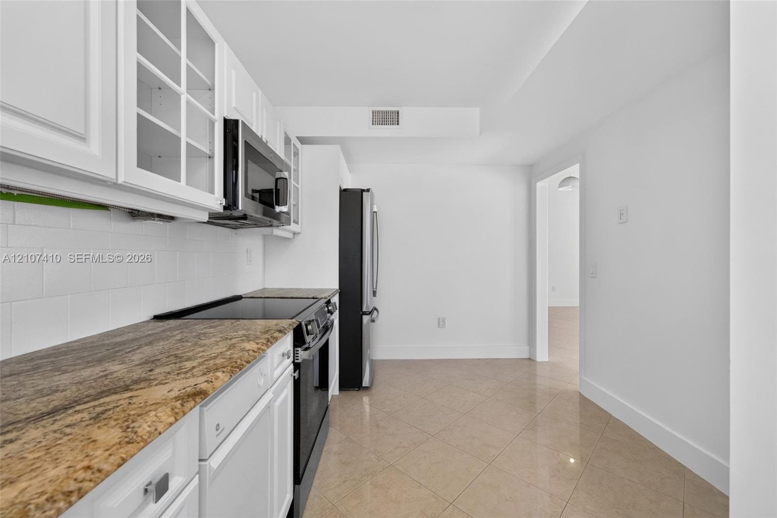 Kitchen featuring white cabinetry with glass-panel upper doors, stone-finish countertops, white subway tile backsplash, and stainless steel appliances, set against ceramic tile flooring