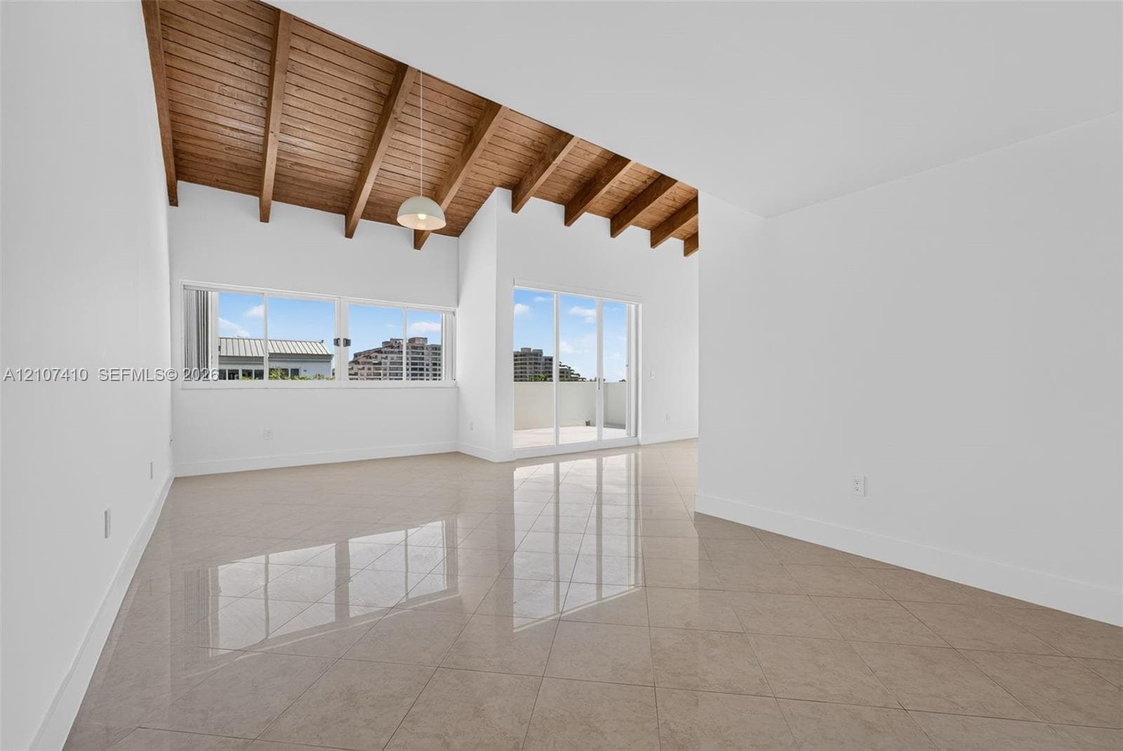 Vaulted ceilings with exposed wooden beams, large-format tile flooring, oversized windows, and glass sliding doors providing exterior access