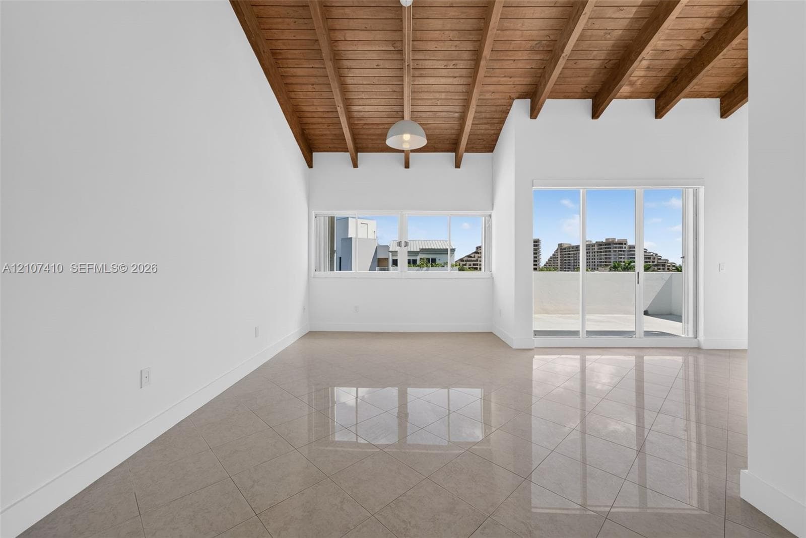 Vaulted ceilings with exposed wooden beams, polished tile flooring, pendant lighting, expansive window placement, and sliding glass doors