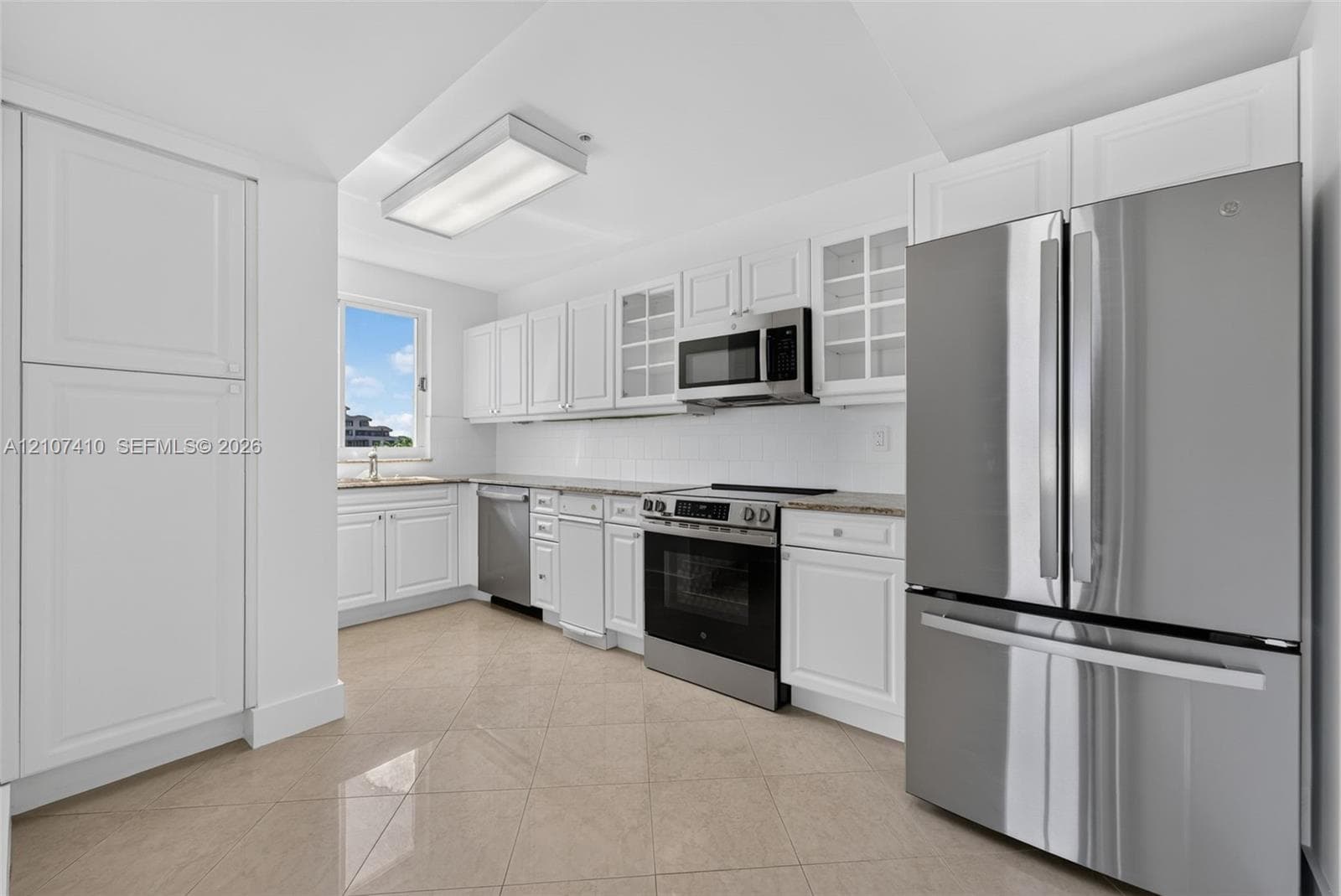 Kitchen featuring white cabinetry with glass-front accents, stone-composite countertops, stainless steel appliances, and large-format tile flooring
