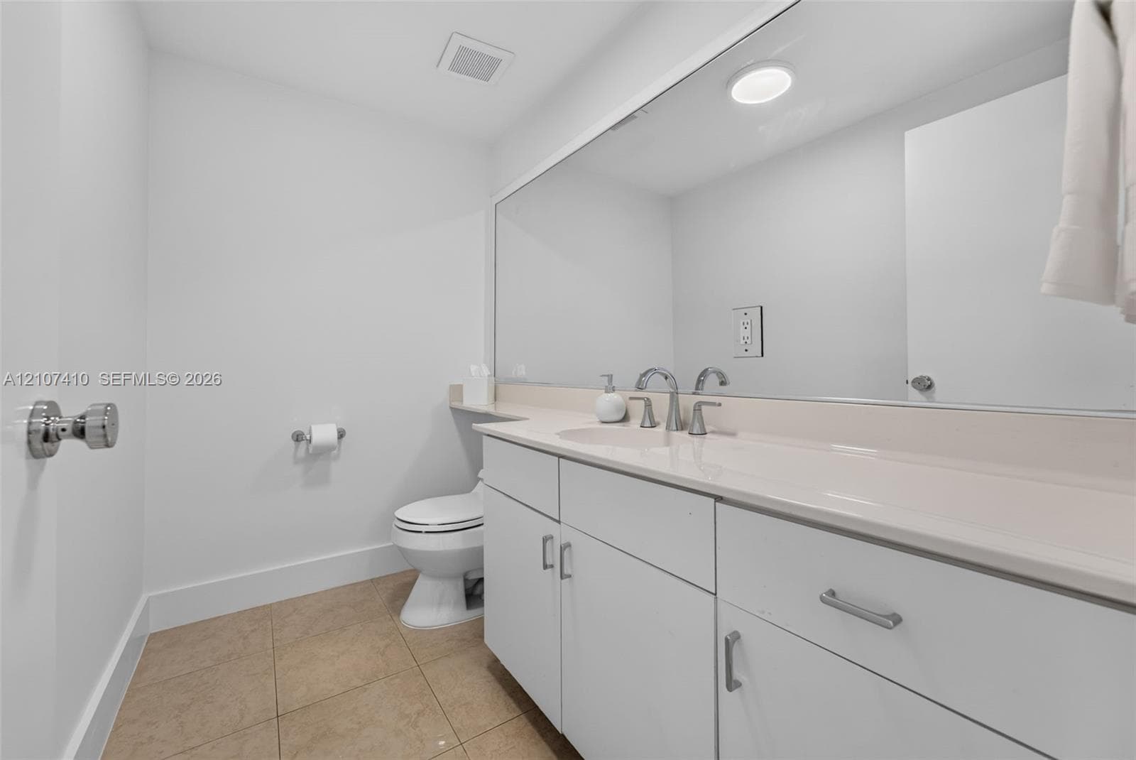Bathroom featuring a white vanity cabinet, solid-surface countertop with an integrated sink, full-width mirror, and tile flooring