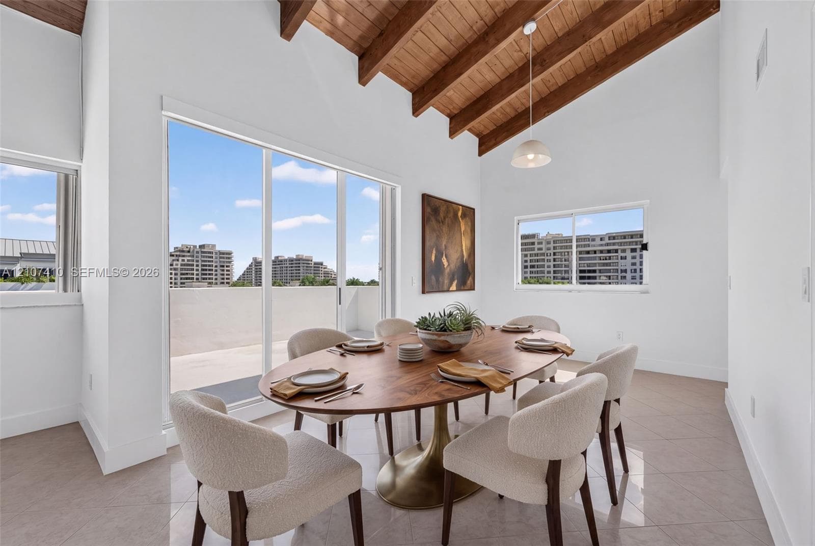 Vaulted ceiling with exposed wood beams, sliding glass doors to exterior balcony, tile flooring, and large window wall