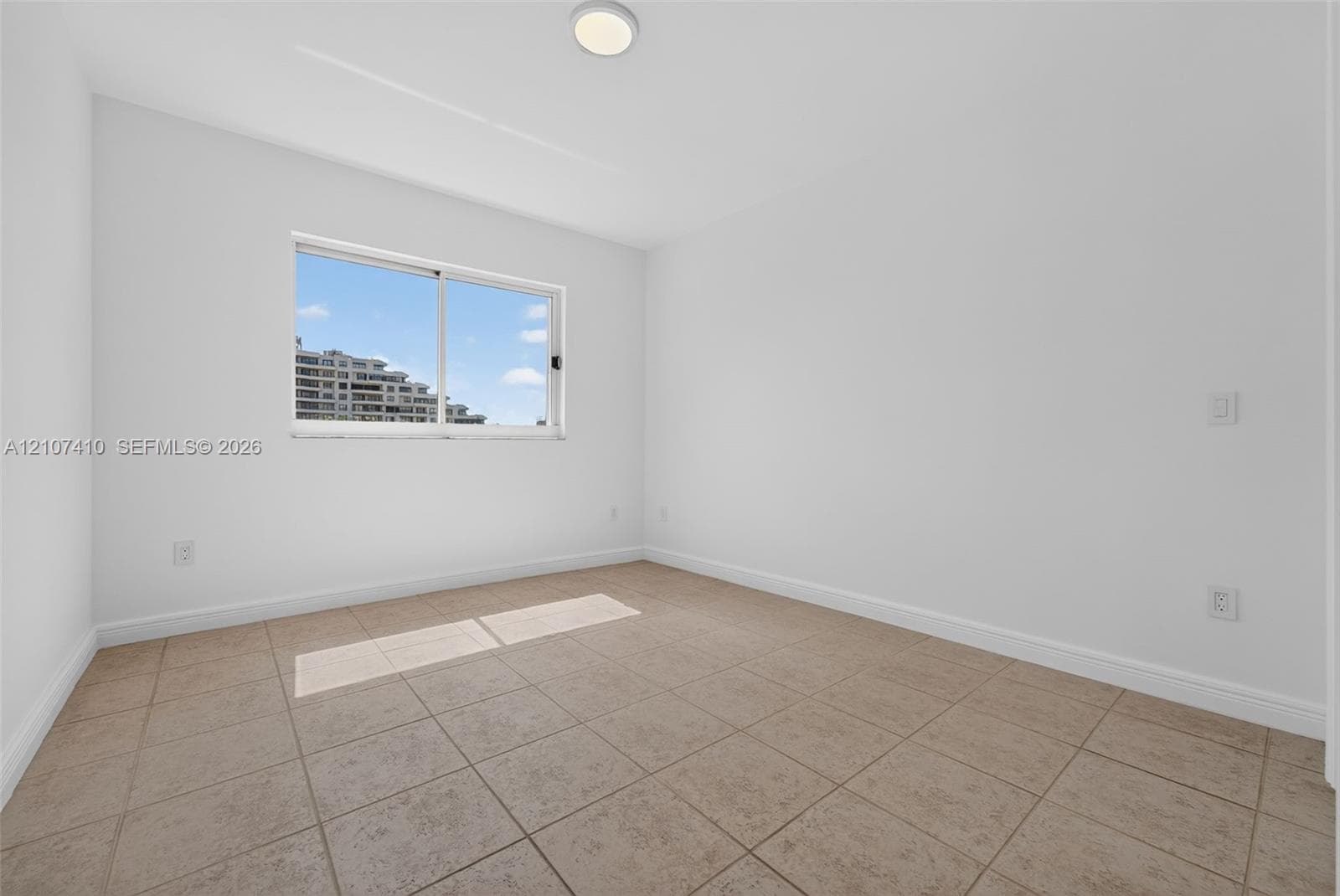 Neutral interior space featuring tile flooring, smooth white walls, a sliding window, and a flush-mount ceiling fixture