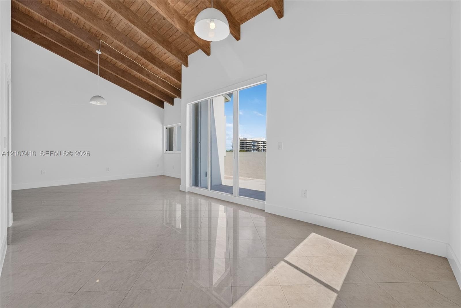 Vaulted ceilings with exposed wooden beams, large-format tile flooring, sliding glass patio doors, and pendant lighting
