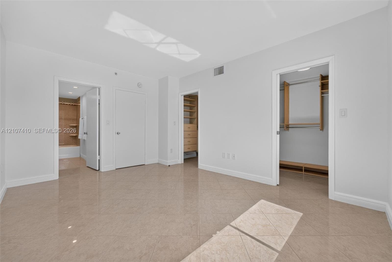 Neutral-toned tile flooring, recessed ceiling lighting, and walk-in closets featuring built-in wooden shelving and drawers