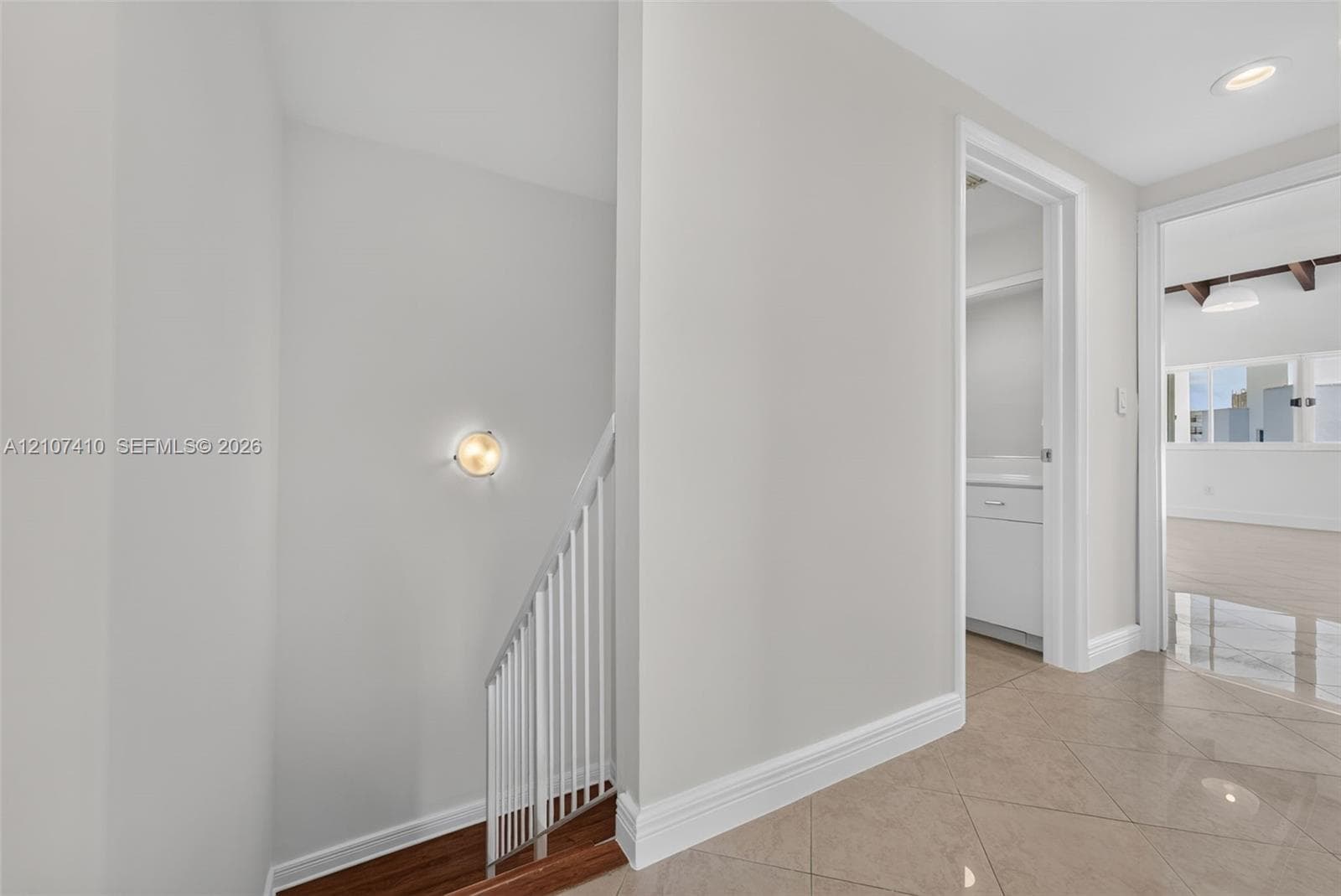 Neutral-toned walls, recessed lighting, polished tile flooring, white metal balustrade, and a circular wall-mounted light fixture