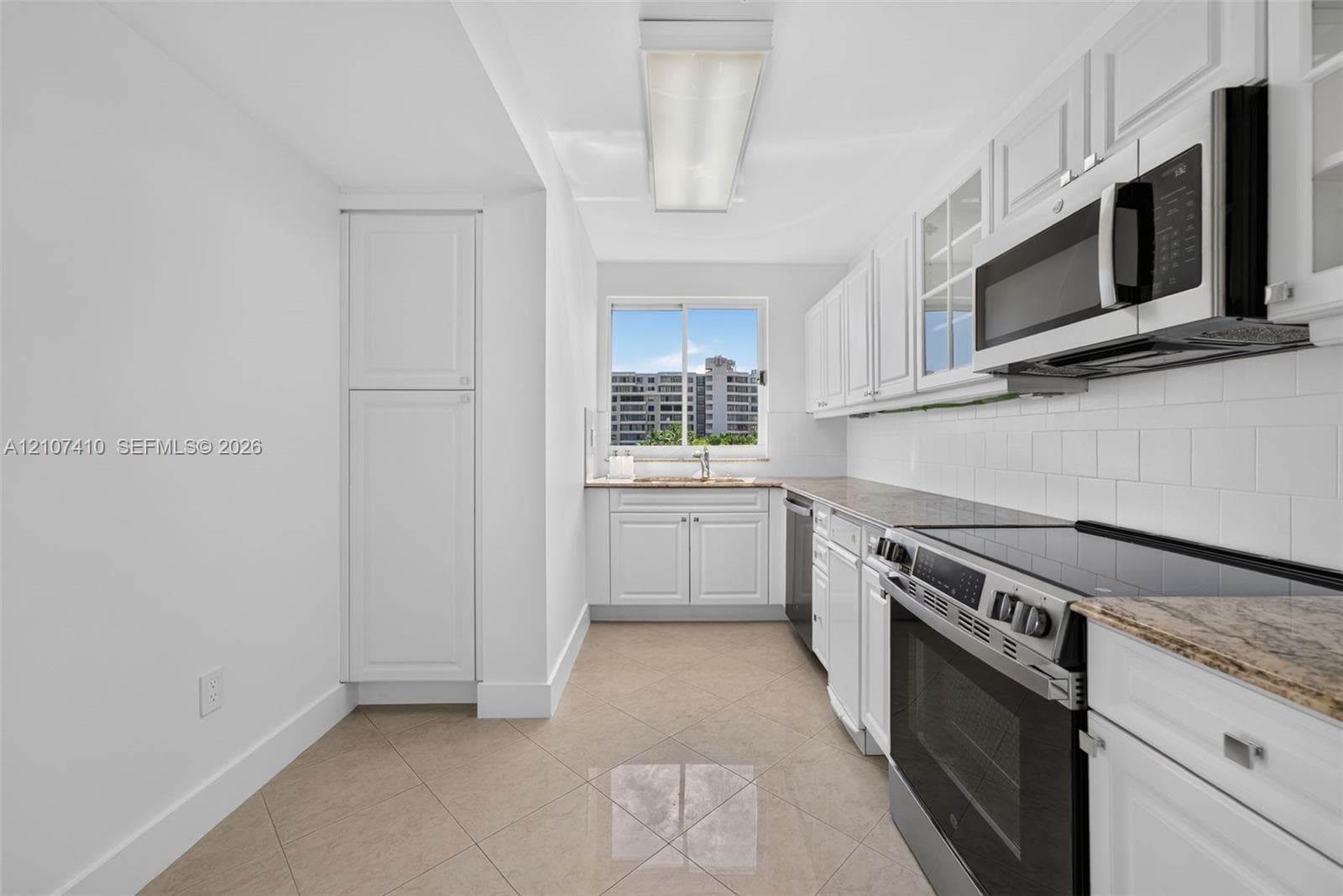 Kitchen featuring white cabinetry, stone countertops, white subway tile backsplash, stainless steel appliances, and tile flooring