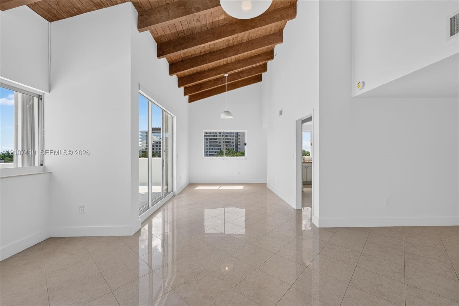Vaulted ceiling featuring exposed wood beams, polished tile flooring, glass sliding doors, and globe pendant lighting