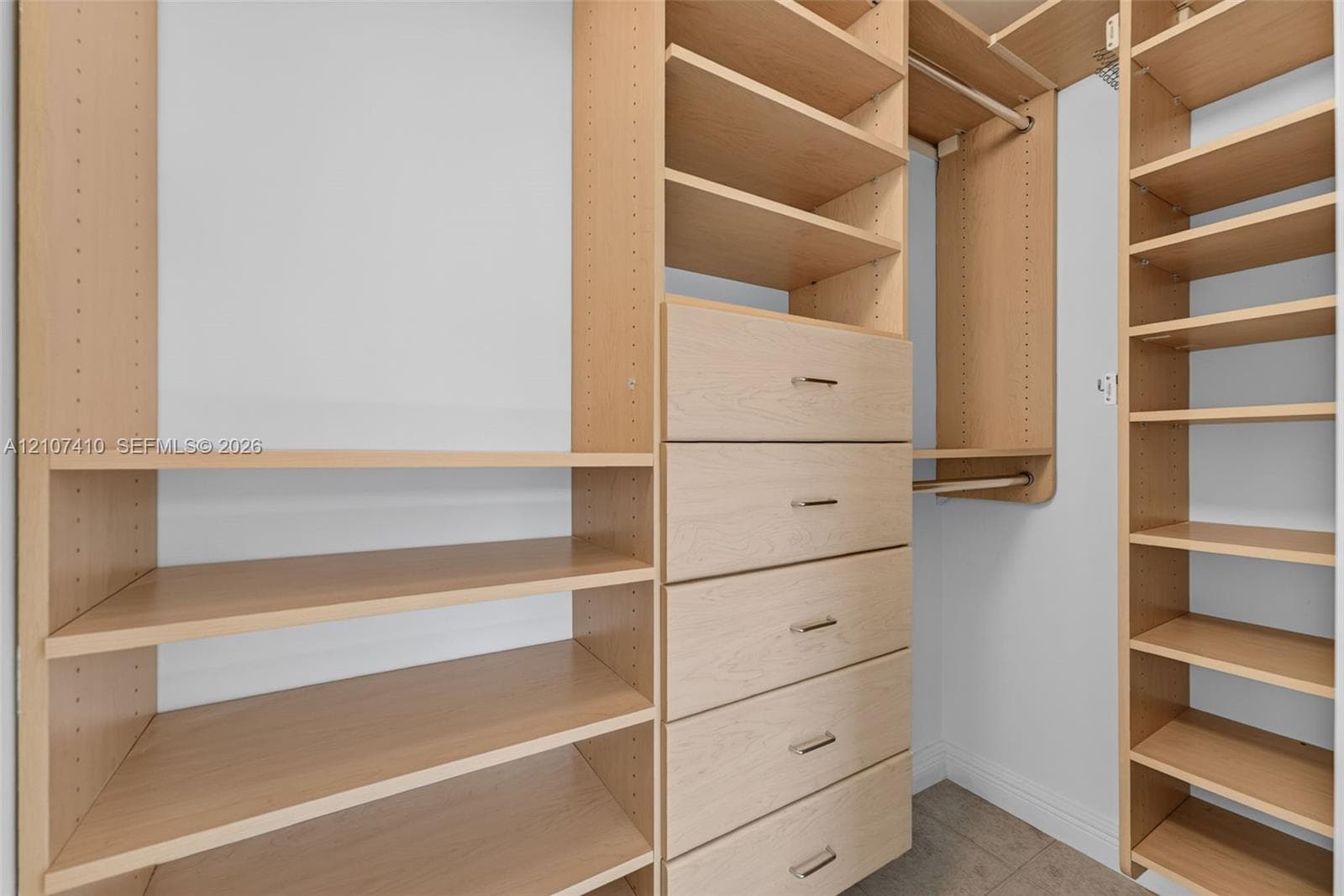 Custom walk-in closet featuring light-toned wood shelving, multiple integrated storage cubbies, a built-in chest of drawers with brushed metal pulls, and double-tier garment rods