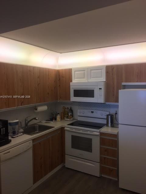 Kitchen featuring wood-finish cabinetry, white appliances, integrated cove lighting, and chevron-patterned tile backsplash