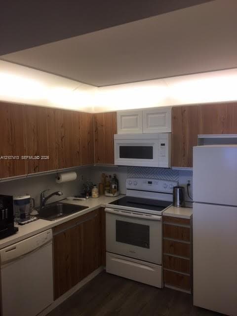 Kitchen featuring wood-finish cabinetry, white appliances, integrated under-cabinet lighting, a chevron-patterned backsplash, and a single-basin stainless steel sink