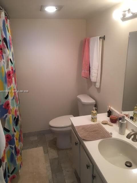 Bathroom featuring a single-basin vanity with a solid-surface countertop, an undermount sink, multi-tone tile flooring, and a wall-mounted light fixture
